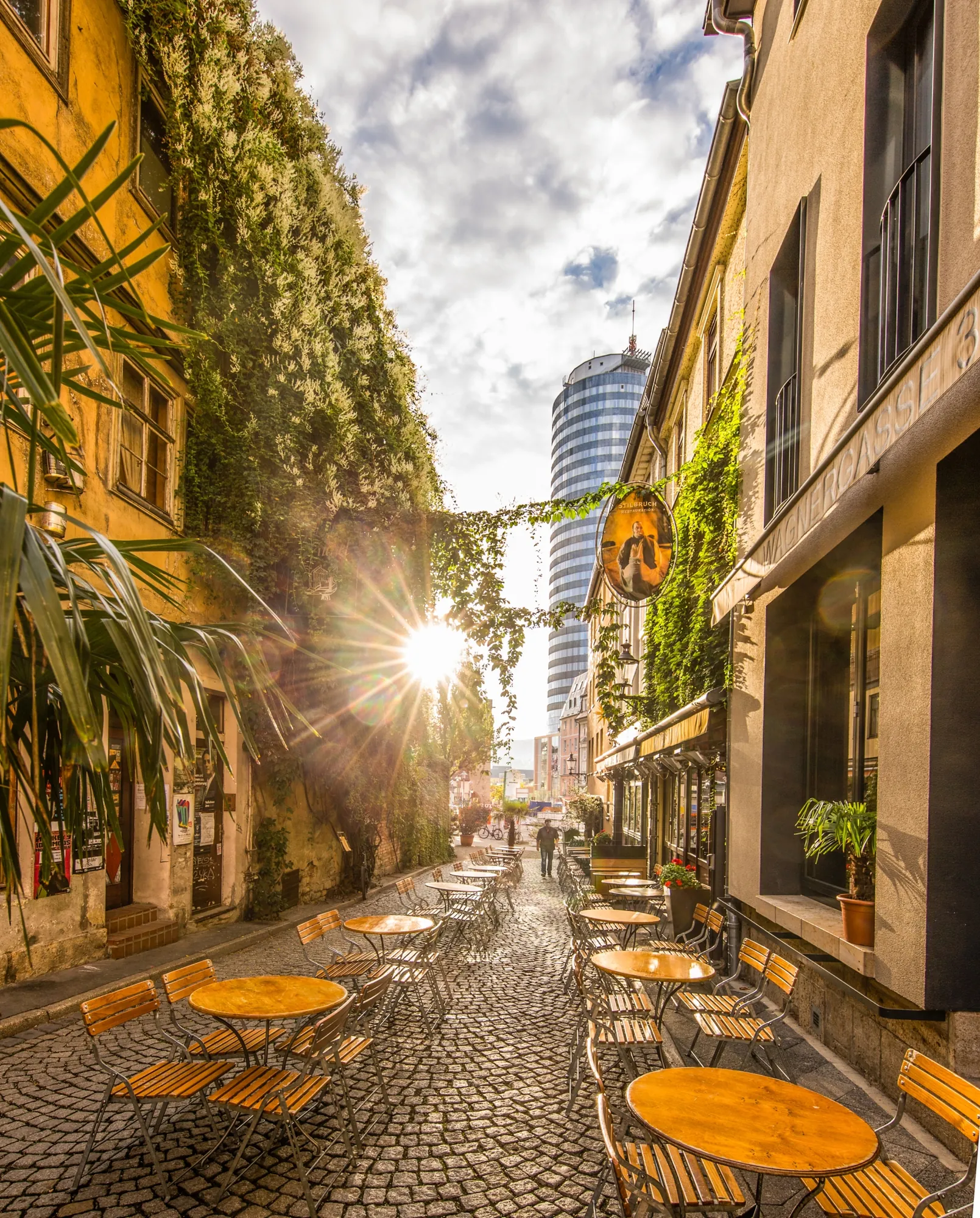 Blick auf gemütliche, zum Verweilen hergerichtete Bistrosets in der Mitte der Wagnergasse von Jena mit begrünten Häuserfassaden.
