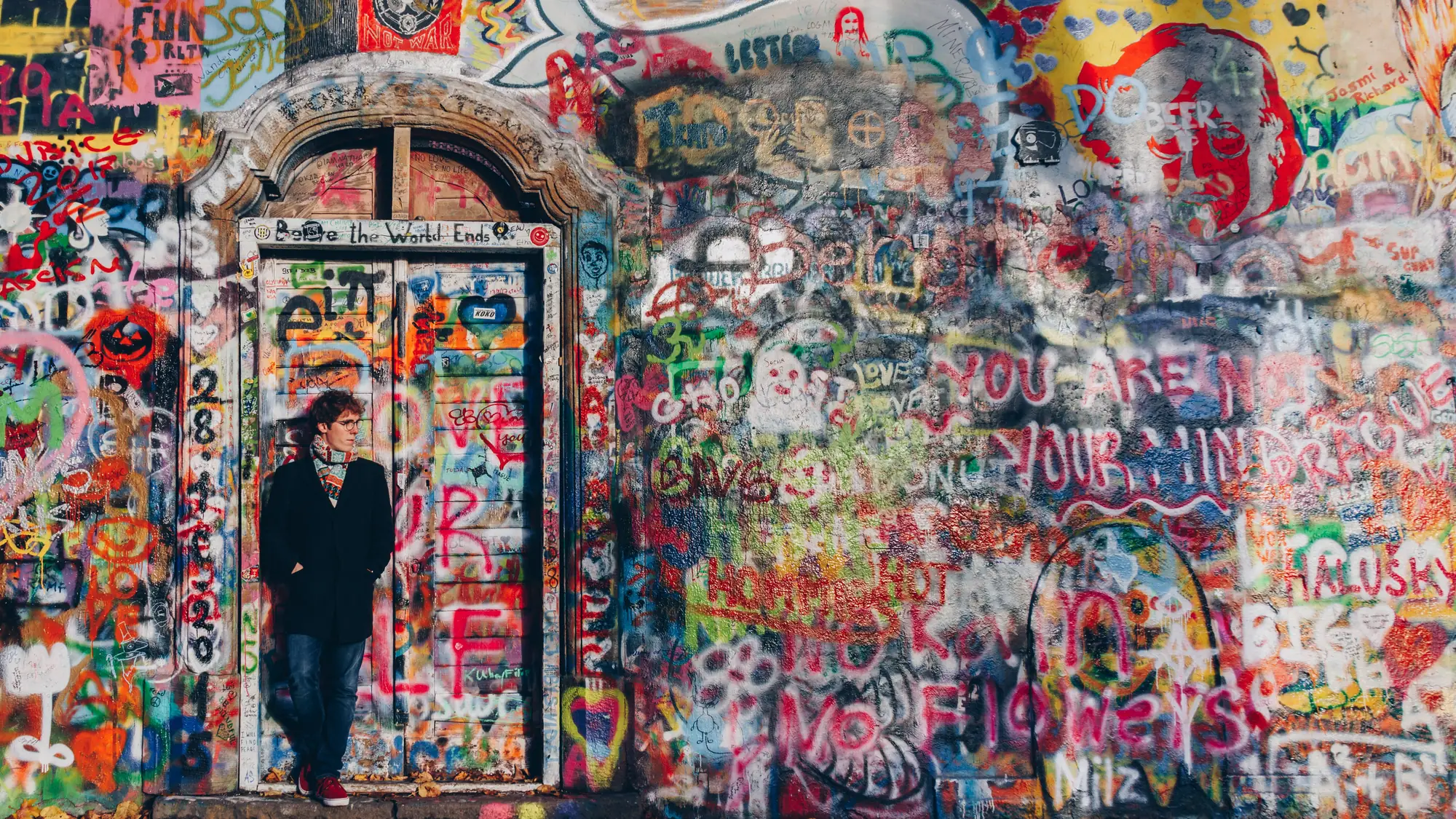 Prag - Denkmal John Lennon Wall - Mann steht vor einer bunten Grafitti-Wand