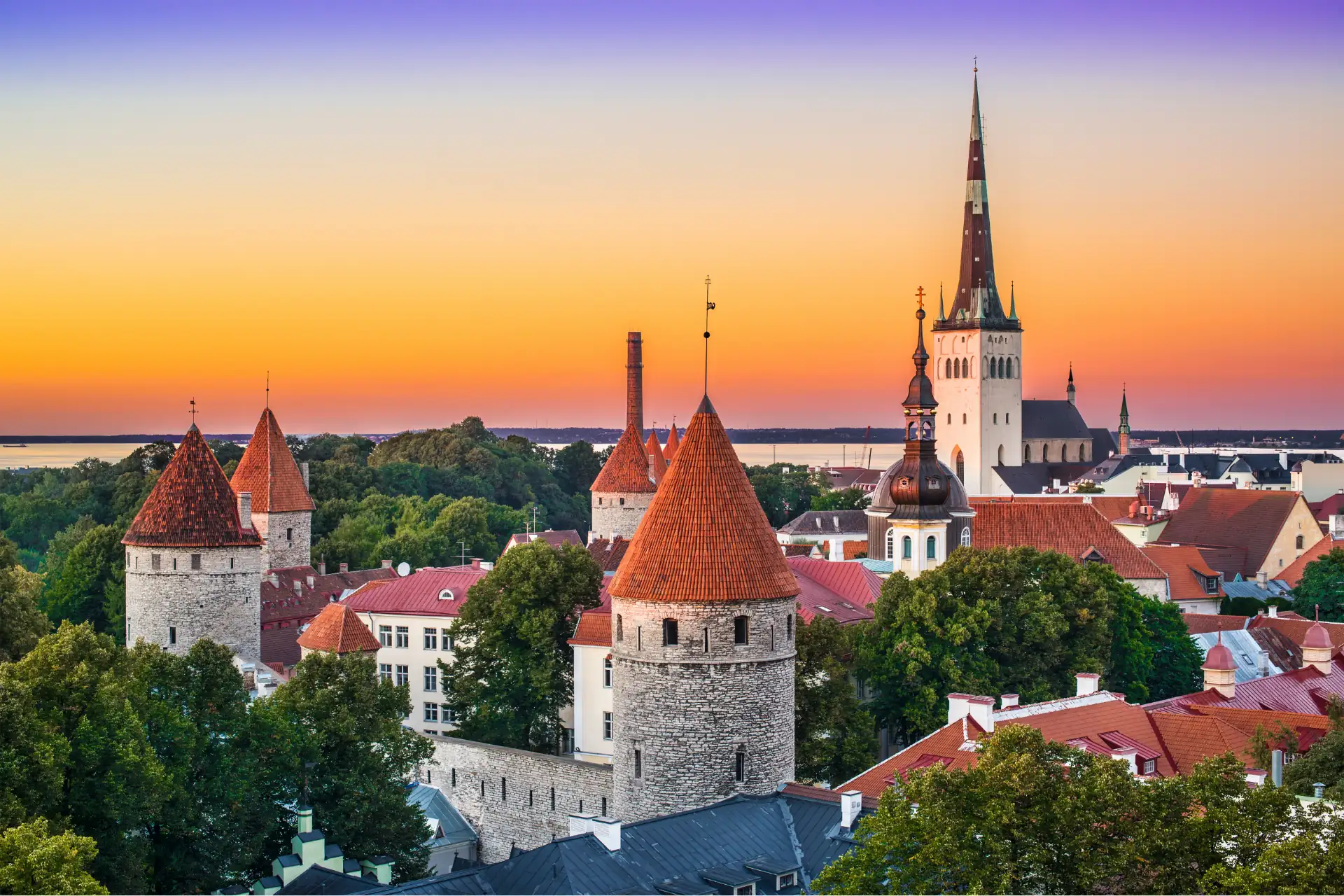 Sonnenuntergang über Tallinns historischer Skyline mit mittelalterlichen Türmen, roten Dächern und der Spitze der St. Olafs-Kirche.