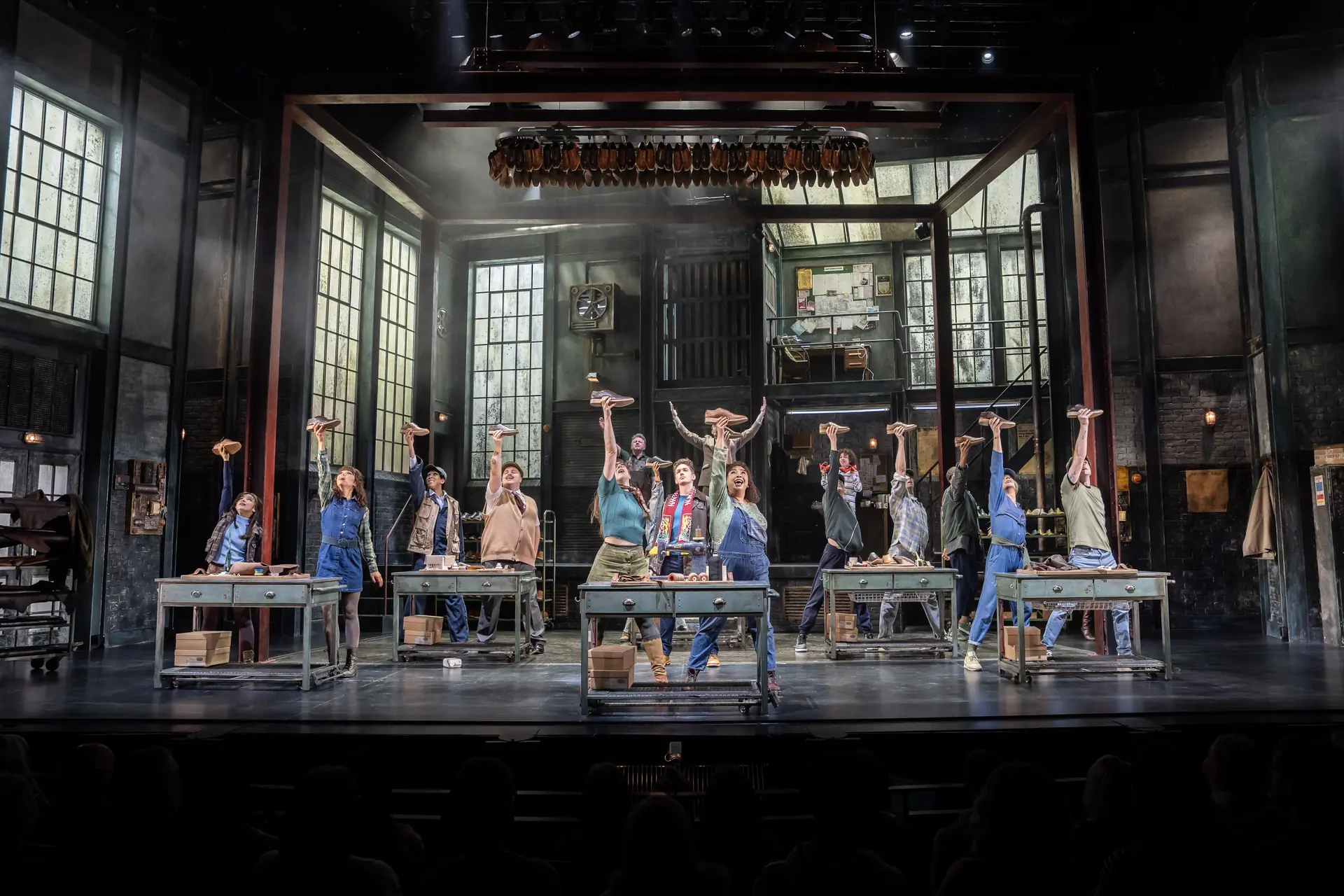 Kinky Boots - The Musical, Szenenbild: Arbeiter in der Schuhfabrik halten Turnschuhe in der Hand hoch.