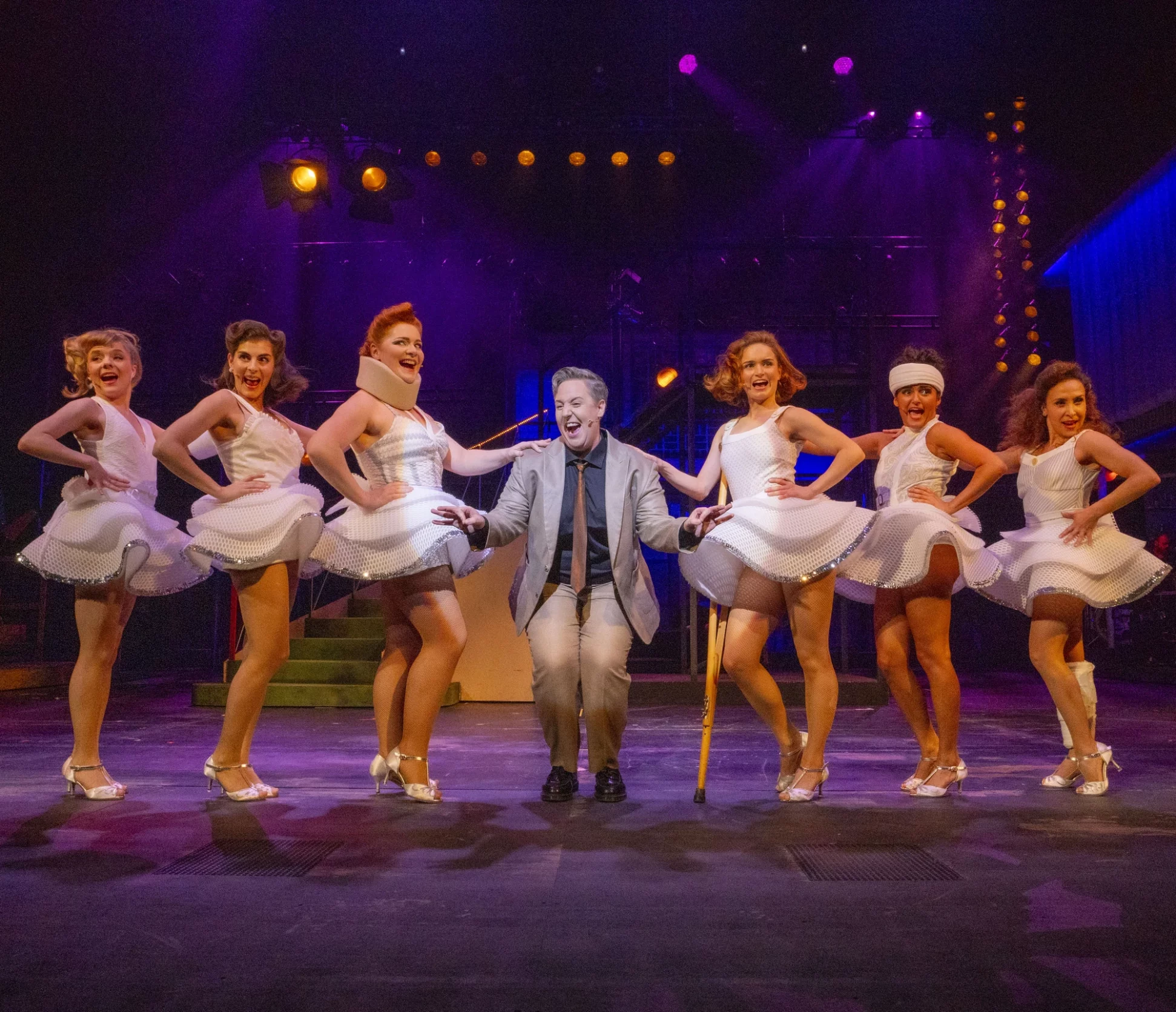 Ensemble von Tänzern und einem männlichen Hauptdarsteller auf einer Theaterbühne.