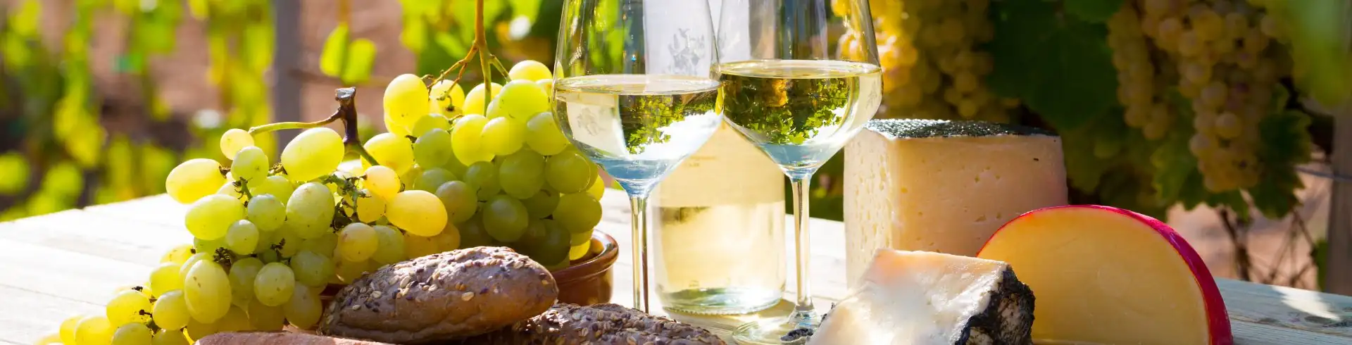 Tisch mit Trauben, Brot, verschiedenen Käsesorten und zwei Gläsern Weißwein im Freien