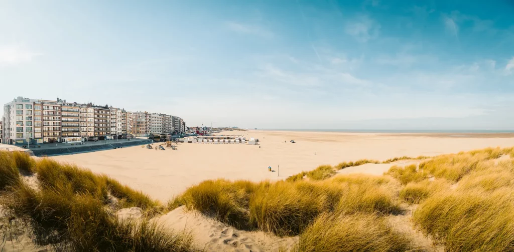 Strand mit Blick aufs Meer und Häuserzeile mit wolkenfreiem Himmel für einen Kurzurlaub Belgien bei Zeebrügge.