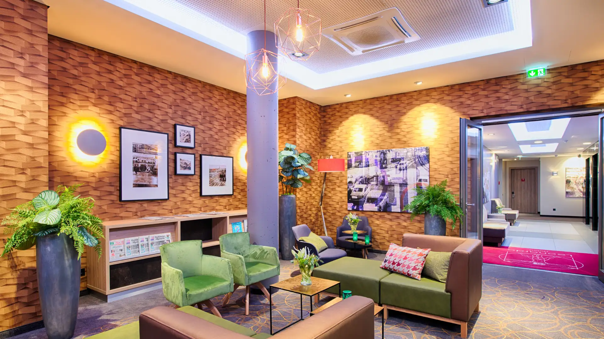 Leonardo Hotels im Kachelformat: Gemütlicher Wartebereich im Leonardo Wolfsburg City mit grünen Sesseln und Sofa, Pflanzen und dekorativen Bildern an der Wand