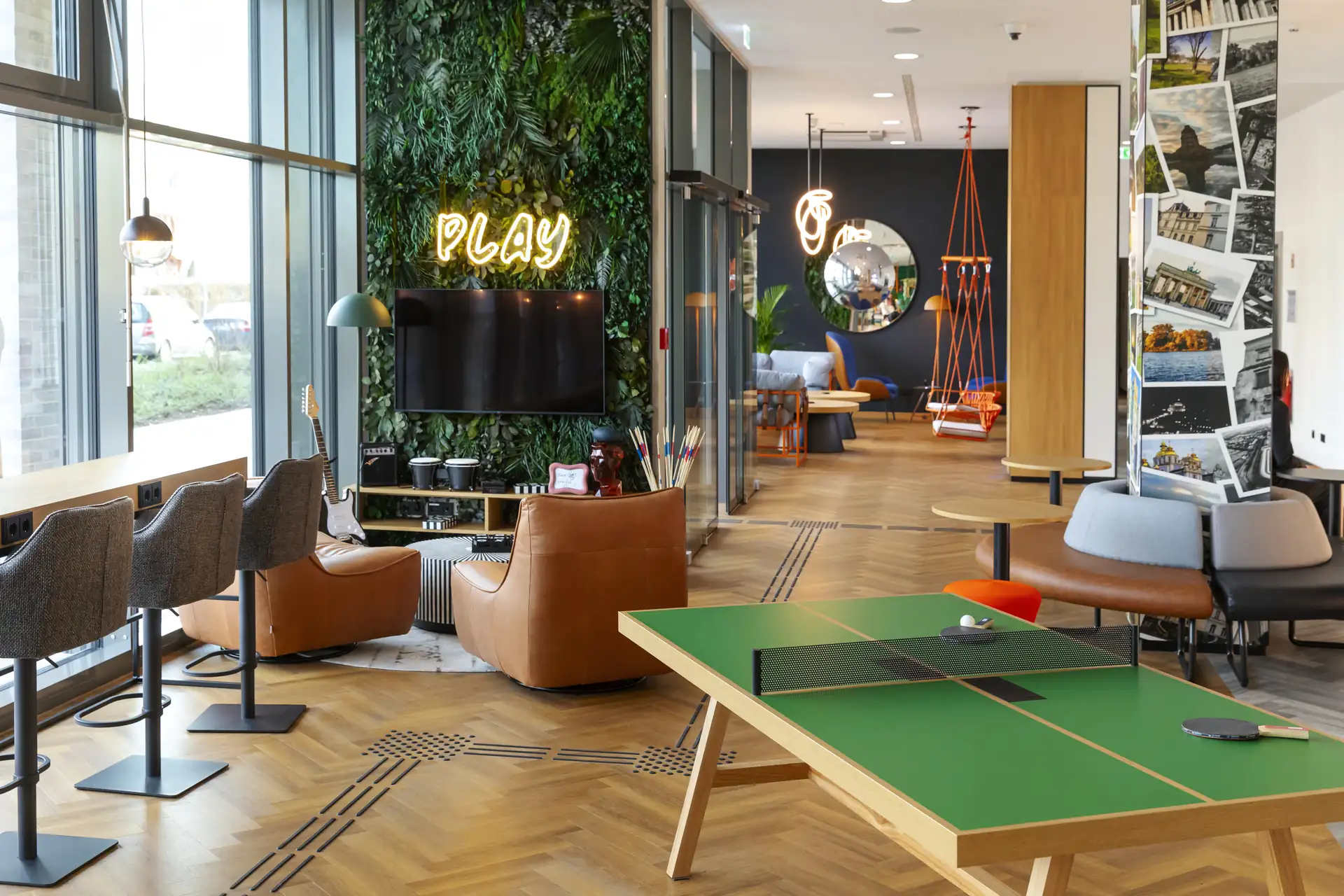 Loginn Hotel Köln Airport: Lobby mit grüner Pflanzenwand, Neonlicht 'PLAY', Tischtennisplatte, Sitzgelegenheiten in verschiedenen Farben und Formen.