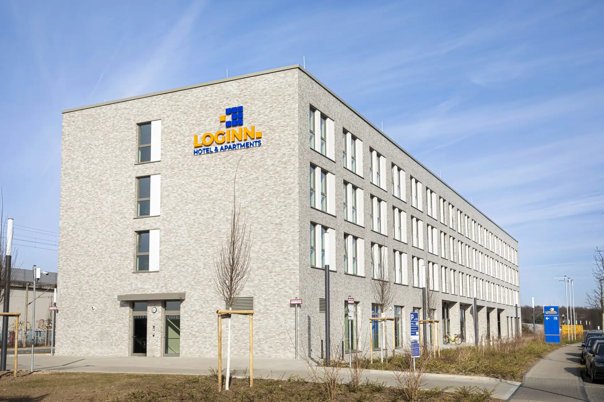 Loginn Hotel Köln Airport: Fassade des LOGINN Hotels und Apartments in Köln, fünfstöckiges Gebäude mit grauer Ziegelsteinoptik, sichtbare Fenster und Eingang.