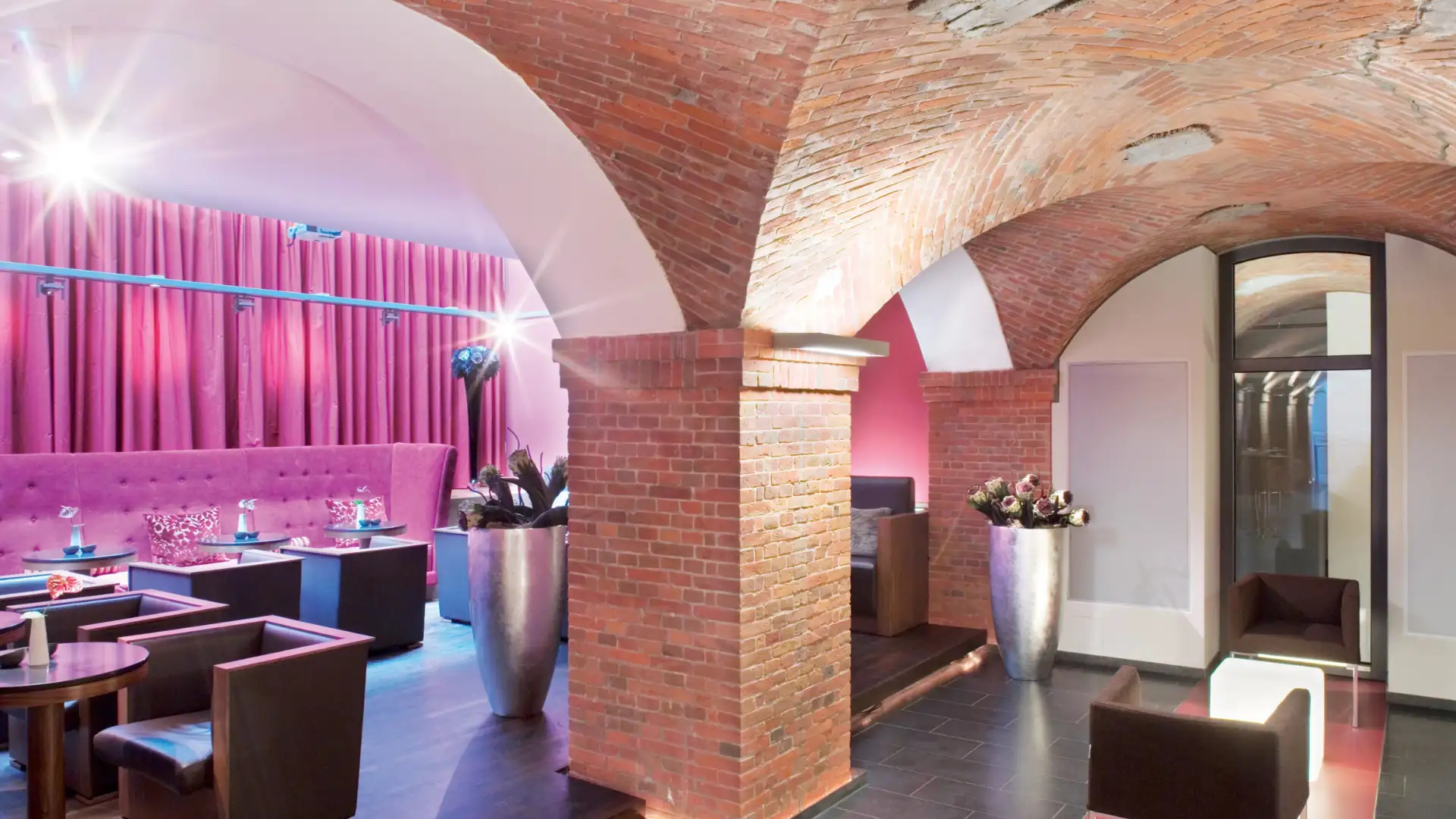 Mövenpick Hotels im Kachelformat: Innenraum des Mövenpick Hotels Hamburg mit gemauerten Rundbögen, rosa Polstermöbeln und Tischen mit Stühlen