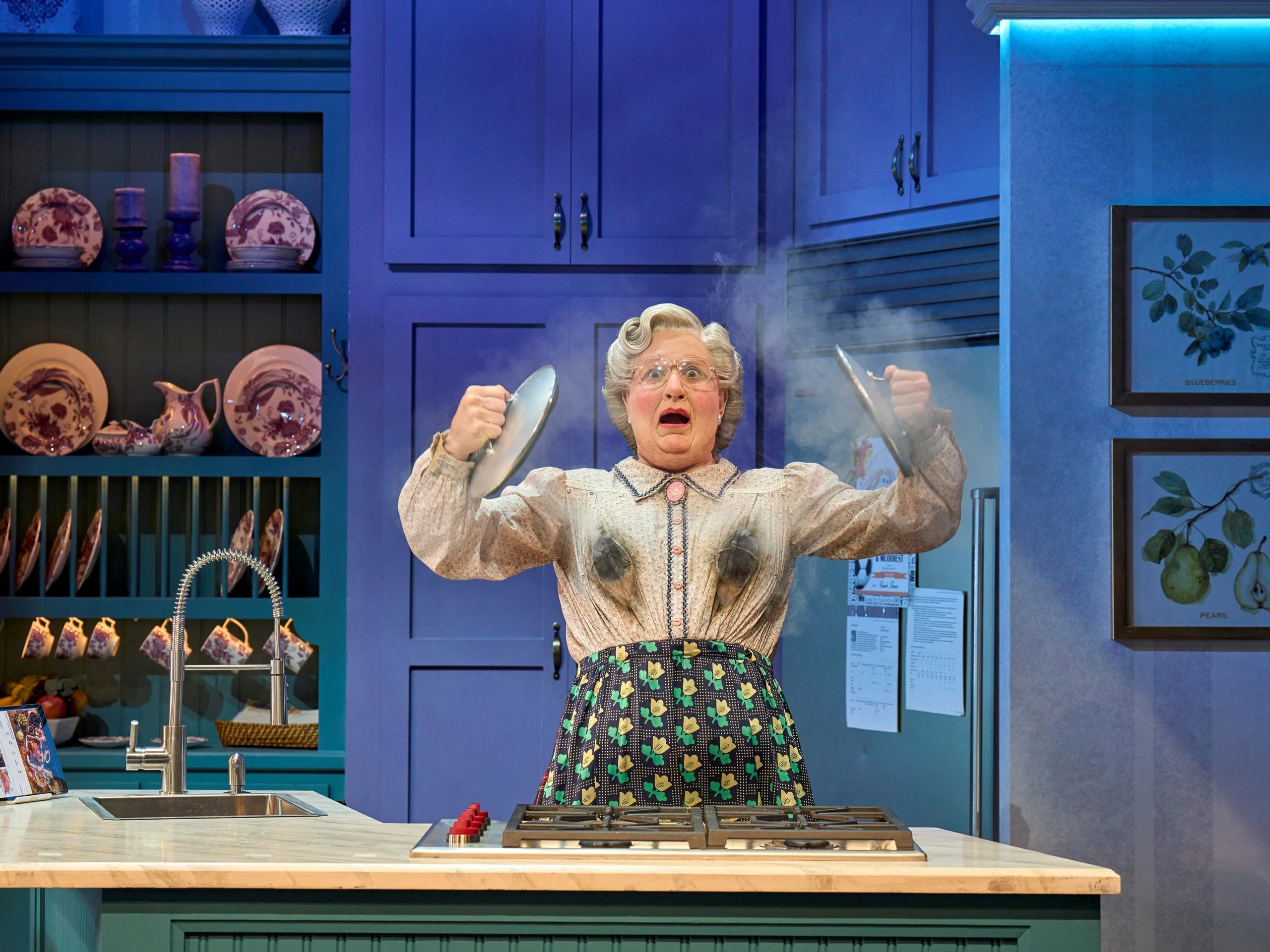Mrs. Doubtfire in einer Schürze kocht in einer modernen Küche.