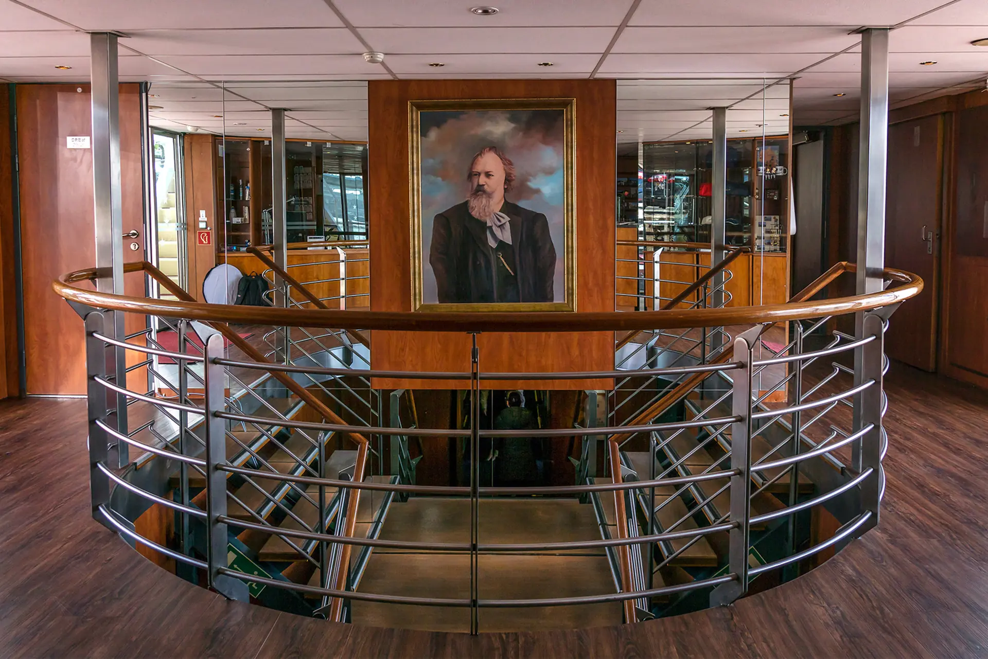 Entree mit Treppen aus Metall und Holz sowie Gemälde von Johannes Brahms im Mittelpunkt der Treppe auf dem Flussschiff MS Johannes Brahms