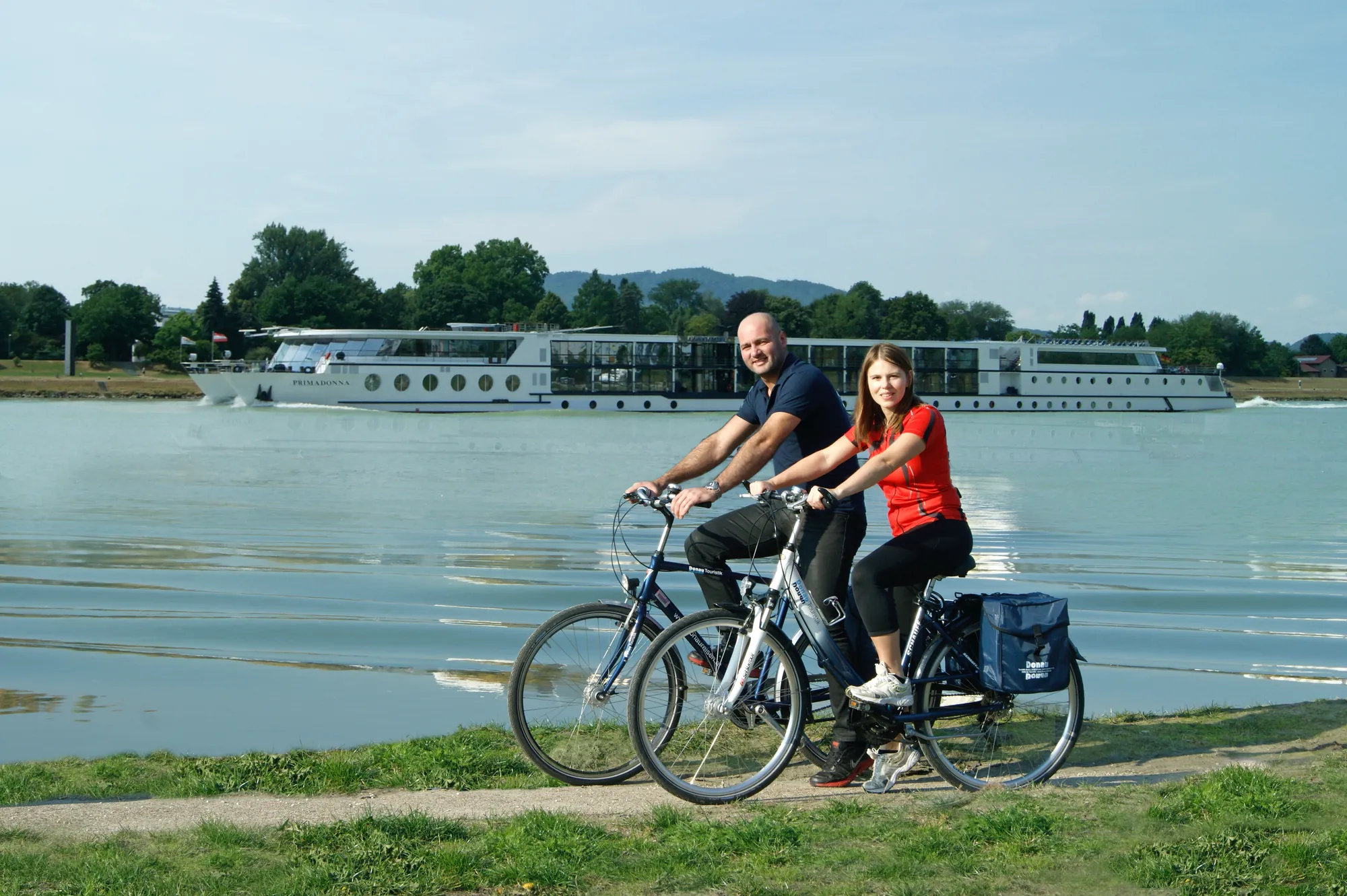 Radler*innen am Ufer der Donau im Hintergrund die MS Primadonna