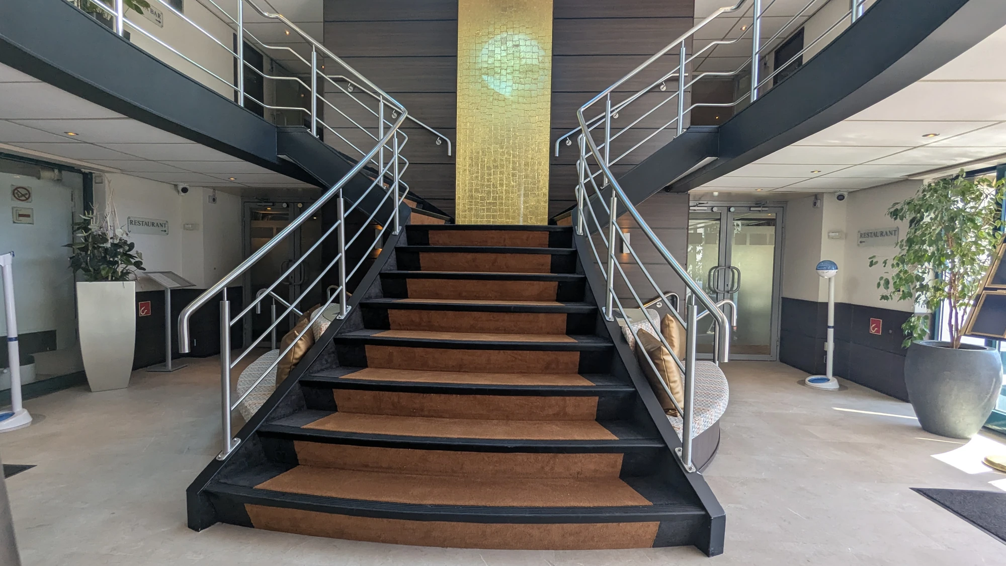 Breite Treppe mit Holzstufen und Metallgeländer in einem modernen, hellen Innenraum mit Pflanzen und Glaswänden auf der VistaNova