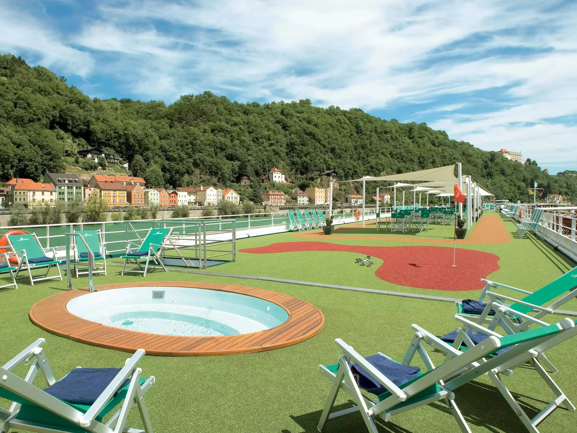 Sonnendeck mit Liegestühlen, kleinem Pool und Minigolfanlage vor bewaldetem Hügel und Häusern auf der VistaNova