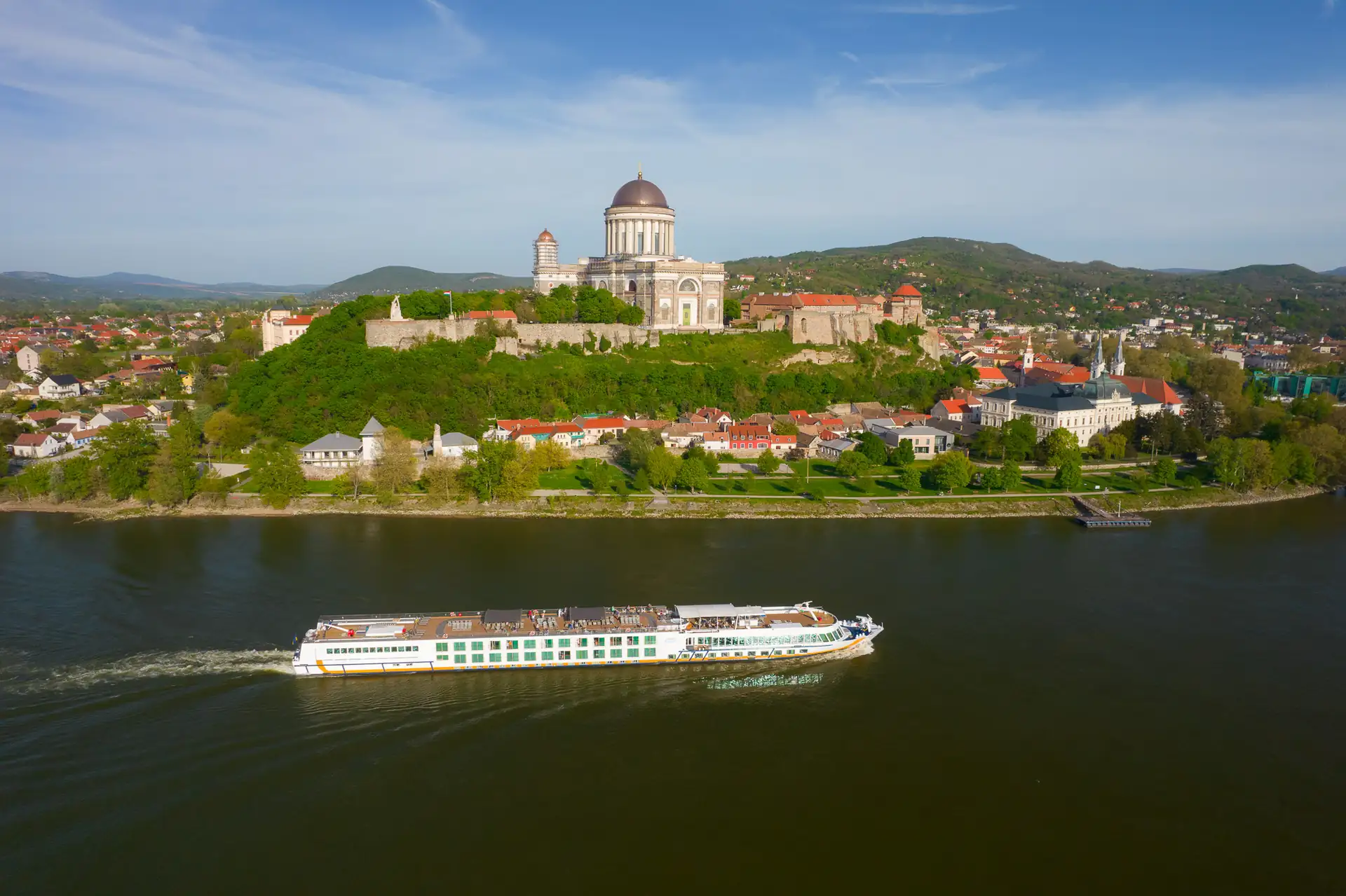 Luftaufnahme der Basilika in Esztergom auf einem bewaldeten Hügel mit Donau im Vordergrund, auf dem die MS VistaSTAR fährt.