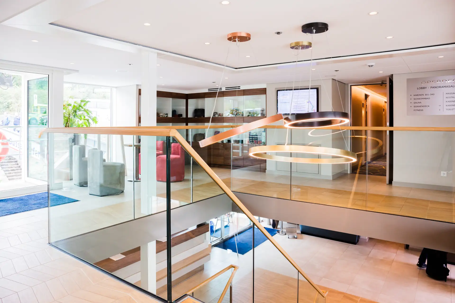 MS VistaSTAR Lobby: Heller Eingangsbereich mit Glasgeländer, Holzhandlauf und modernen runden Deckenleuchten über Treppenaufgang.