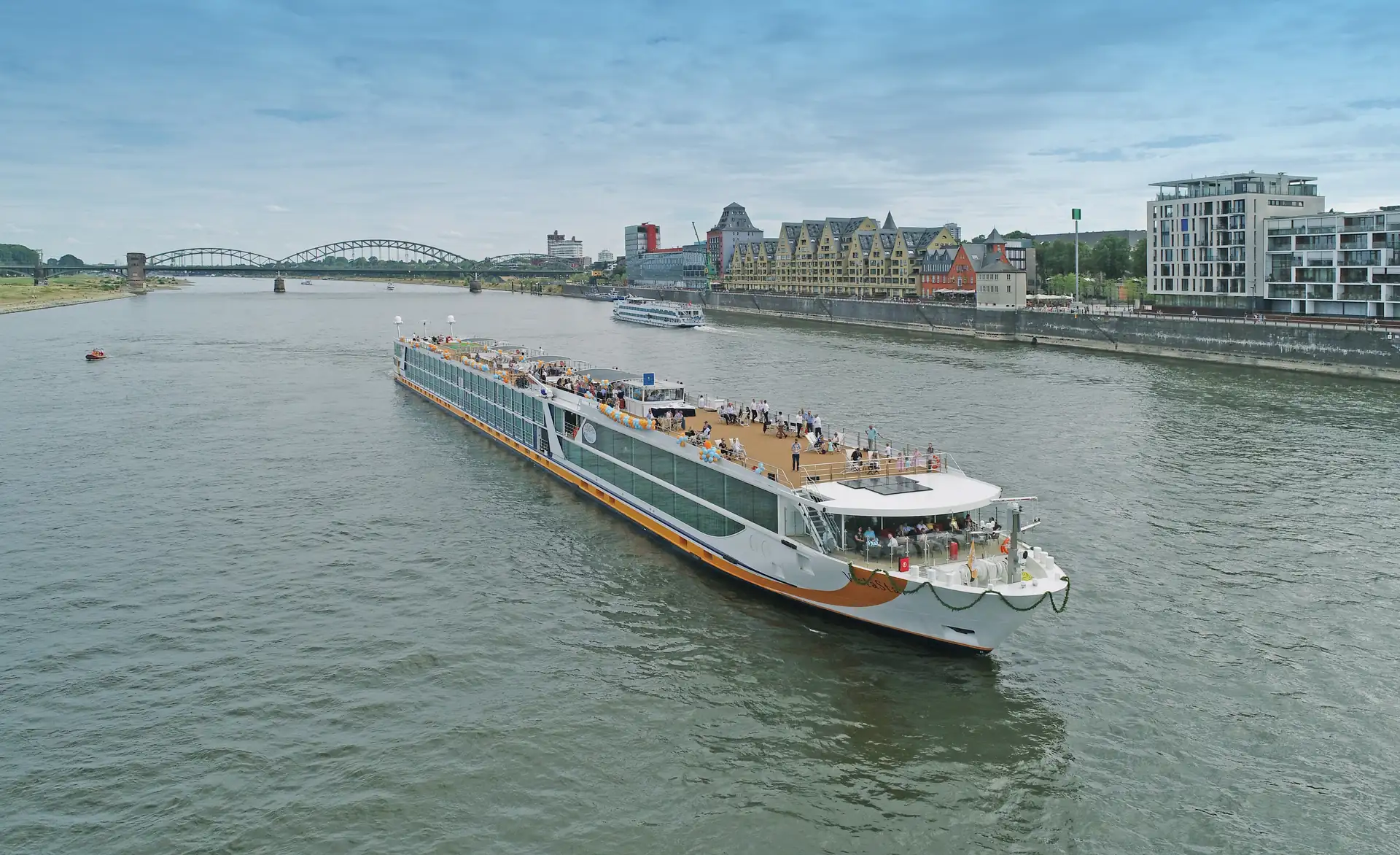 MS VistaSTAR mit offenem Sonnendeck auf breitem Fluss, im Hintergrund Brücke und Stadt mit modernen und historischen Gebäuden.