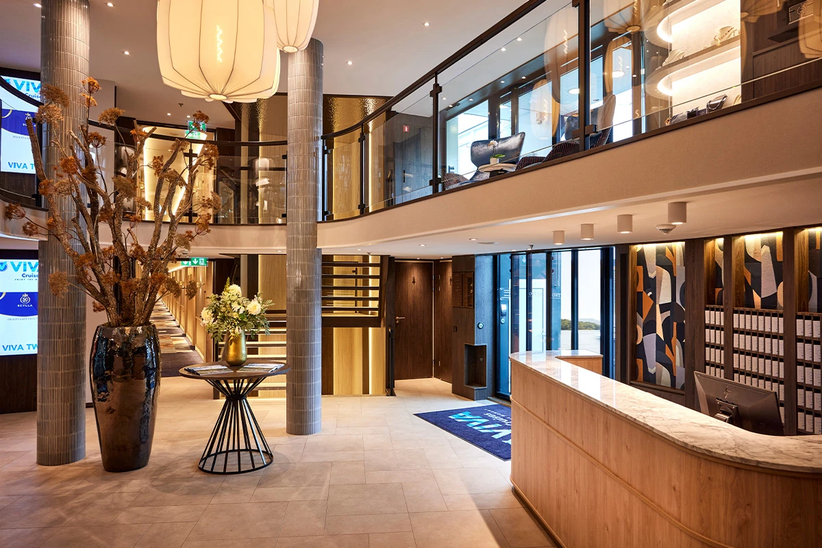 Heller Empfangsbereich mit rundem Tresen, großen Vasen mit Zweigen und Blumen sowie Galerieebene mit Glasgeländer