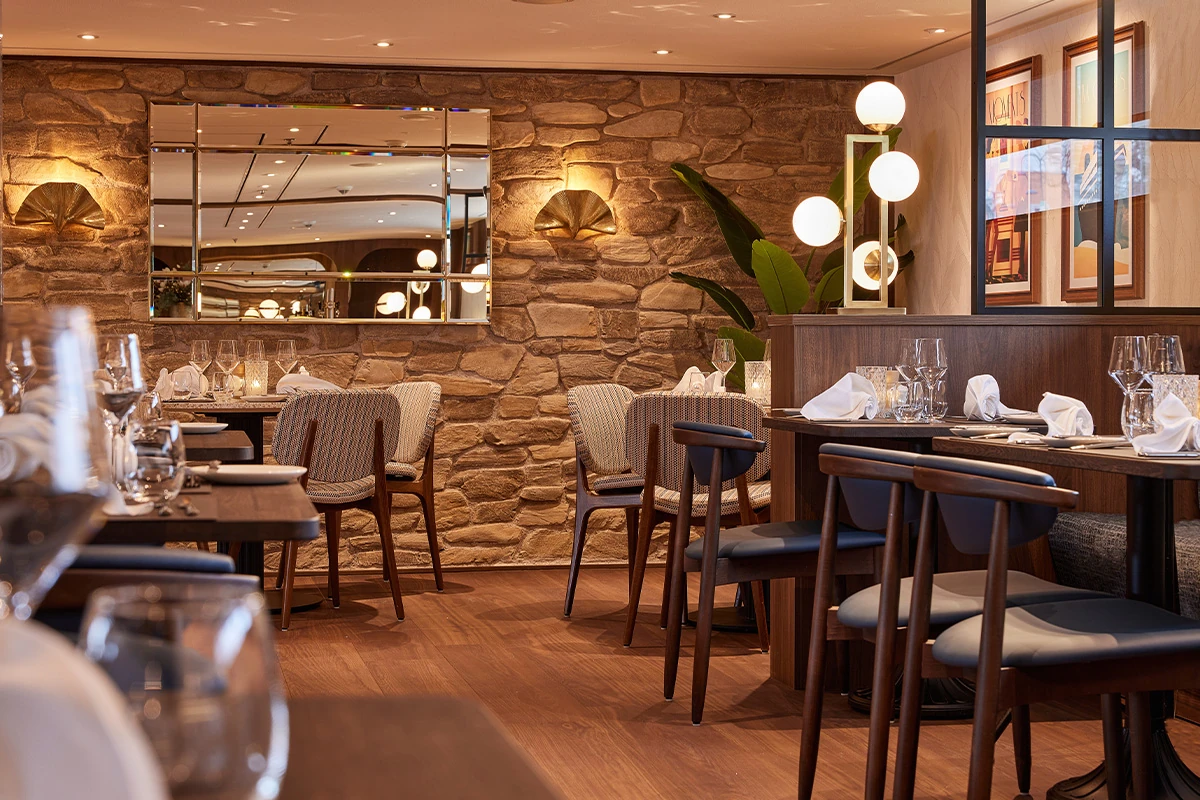 Restaurant mit Holzwänden, Holzboden, mehreren gedeckten Tischen und Stühlen sowie runden Wandlampen