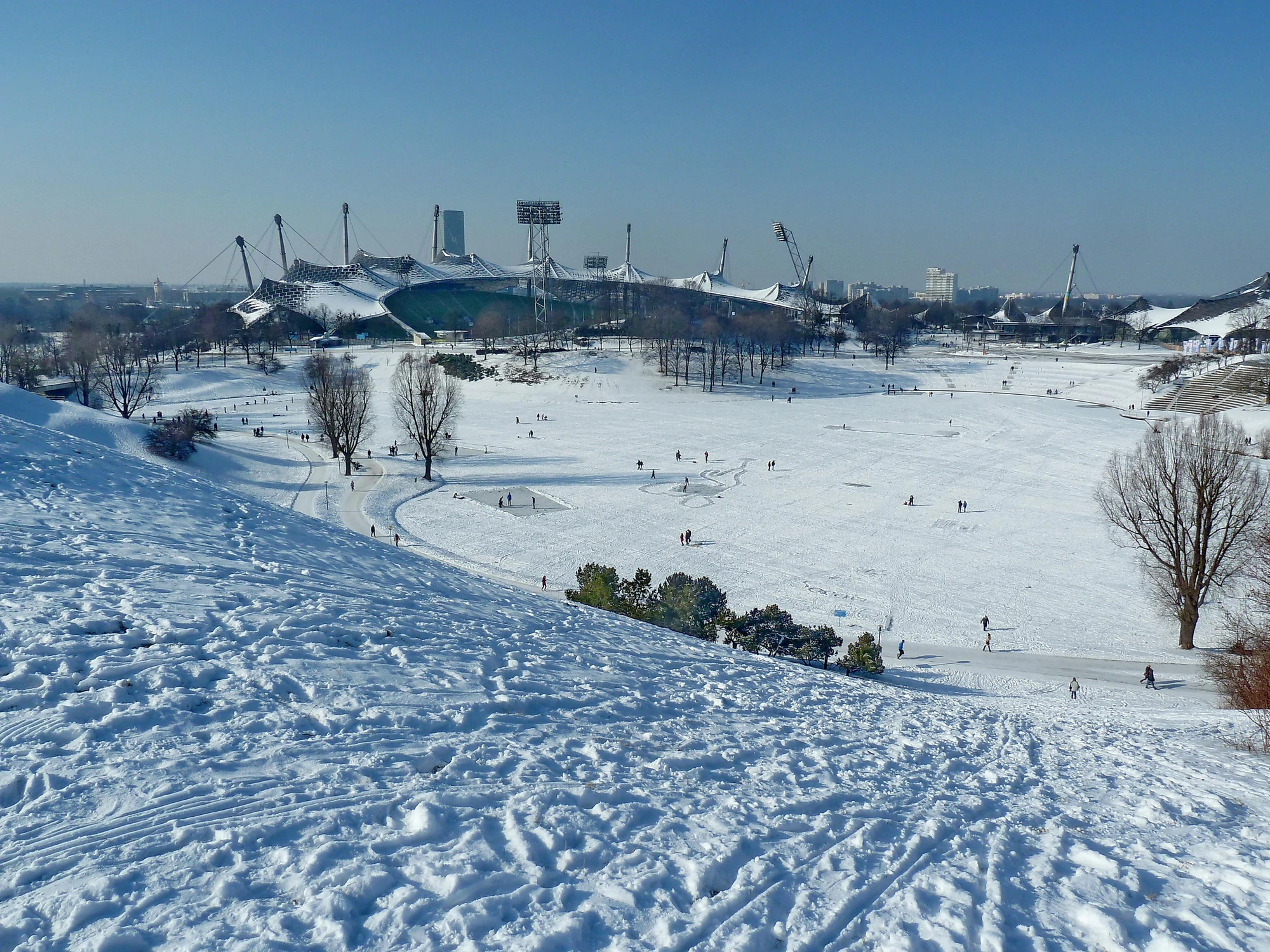 Blick auf den Olympiapark wo Menschen auf einem Platz Schlittschuh laufen
