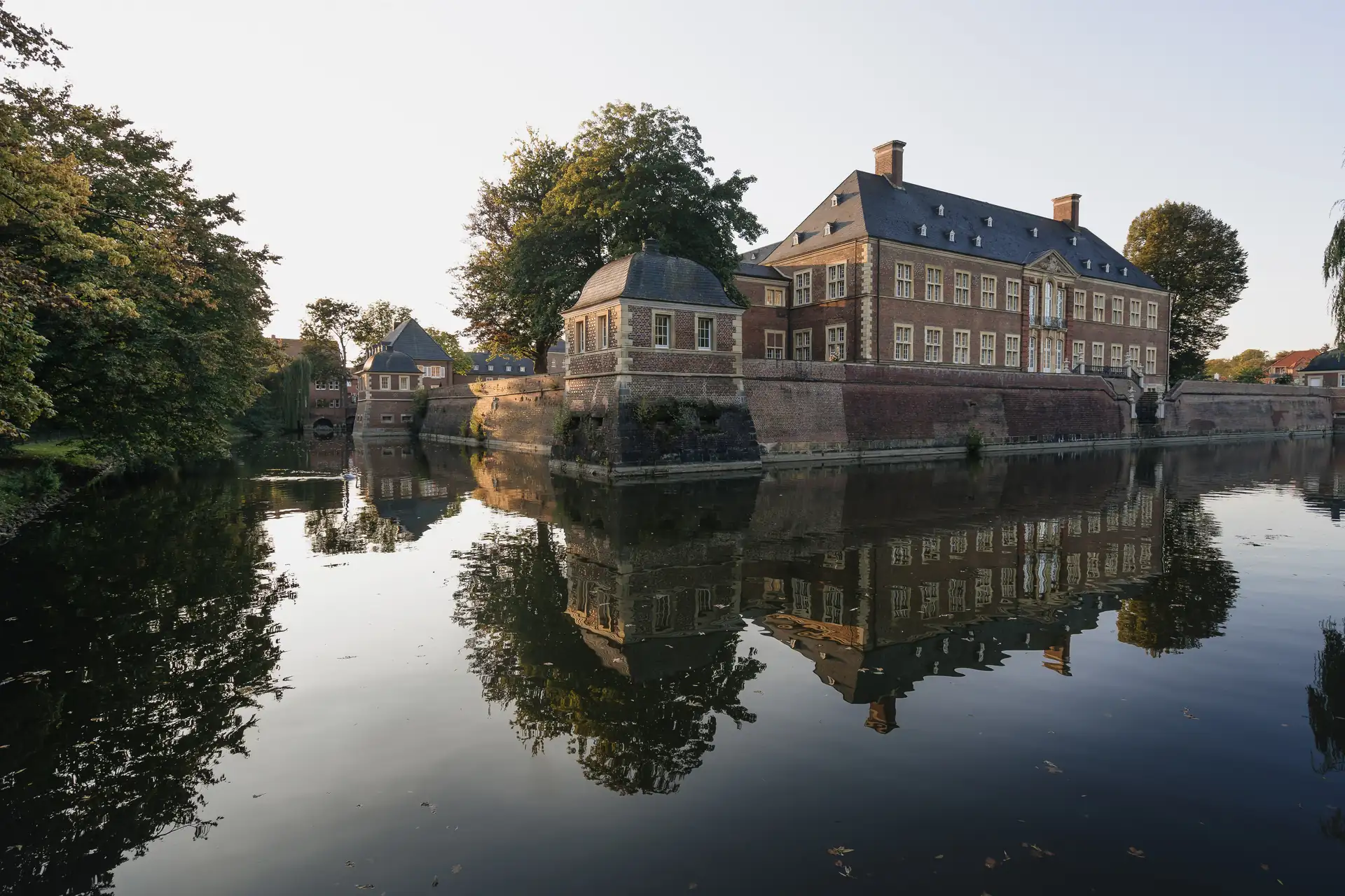 Schloss Ahaus mit Wassergraben und Spiegelung im ruhigen Wasser, umgeben von Bäumen und klarem Himmel