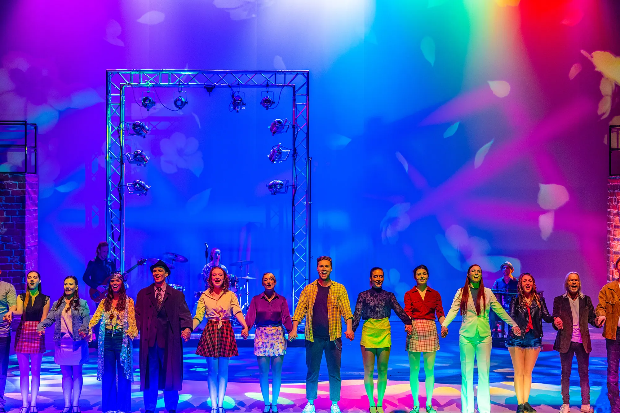 Live-Performance mit Darstellern, die sich auf der Bühne die Hände halten.