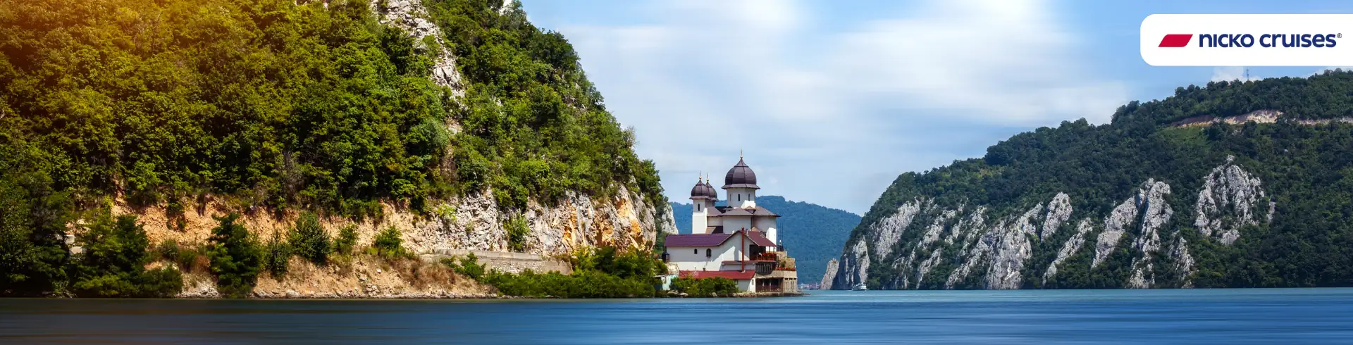 Donau, Eisernes Tor: Flusslandschaft mit bewaldeten Felsen und einer Kirche am Ufer unter blauem Himmel