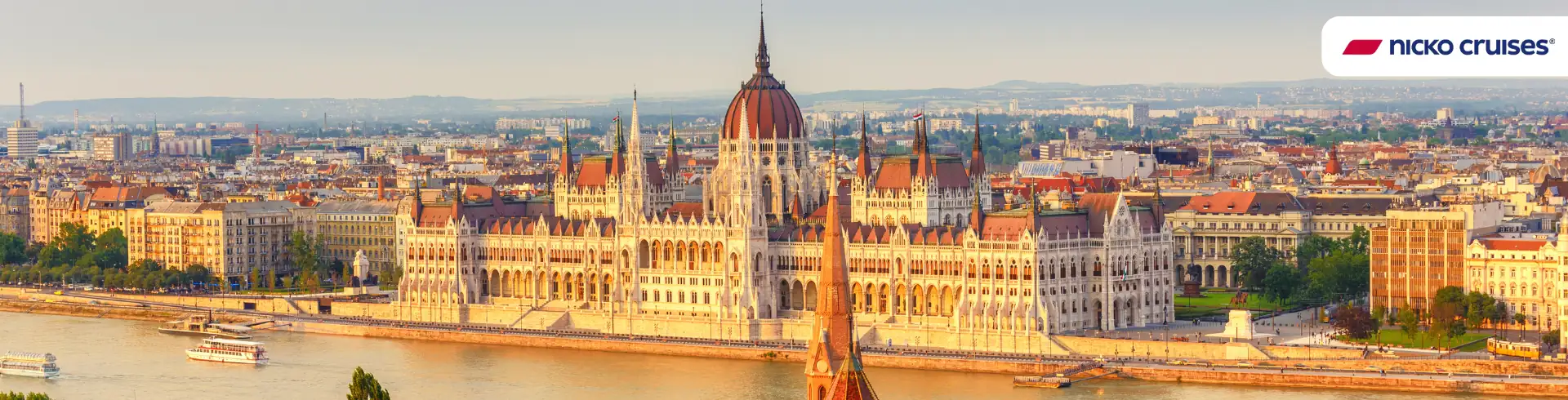 Auktionsbanner nicko cruises Donau-Kreuzfahrt: Blick auf das ungarische Parlament am Donauufer in Budapest bei Tageslicht, mit mehreren Schiffen auf der Donau.