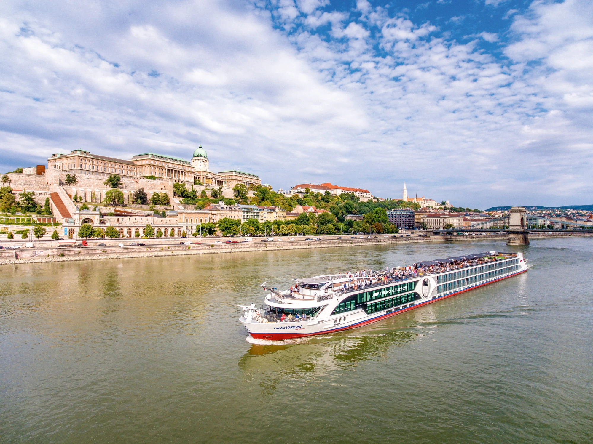 nickoVISION auf der Donau, im Hintergrund ist eine bewaldete Uferlandschaft und historische Gebäude zu sehen.