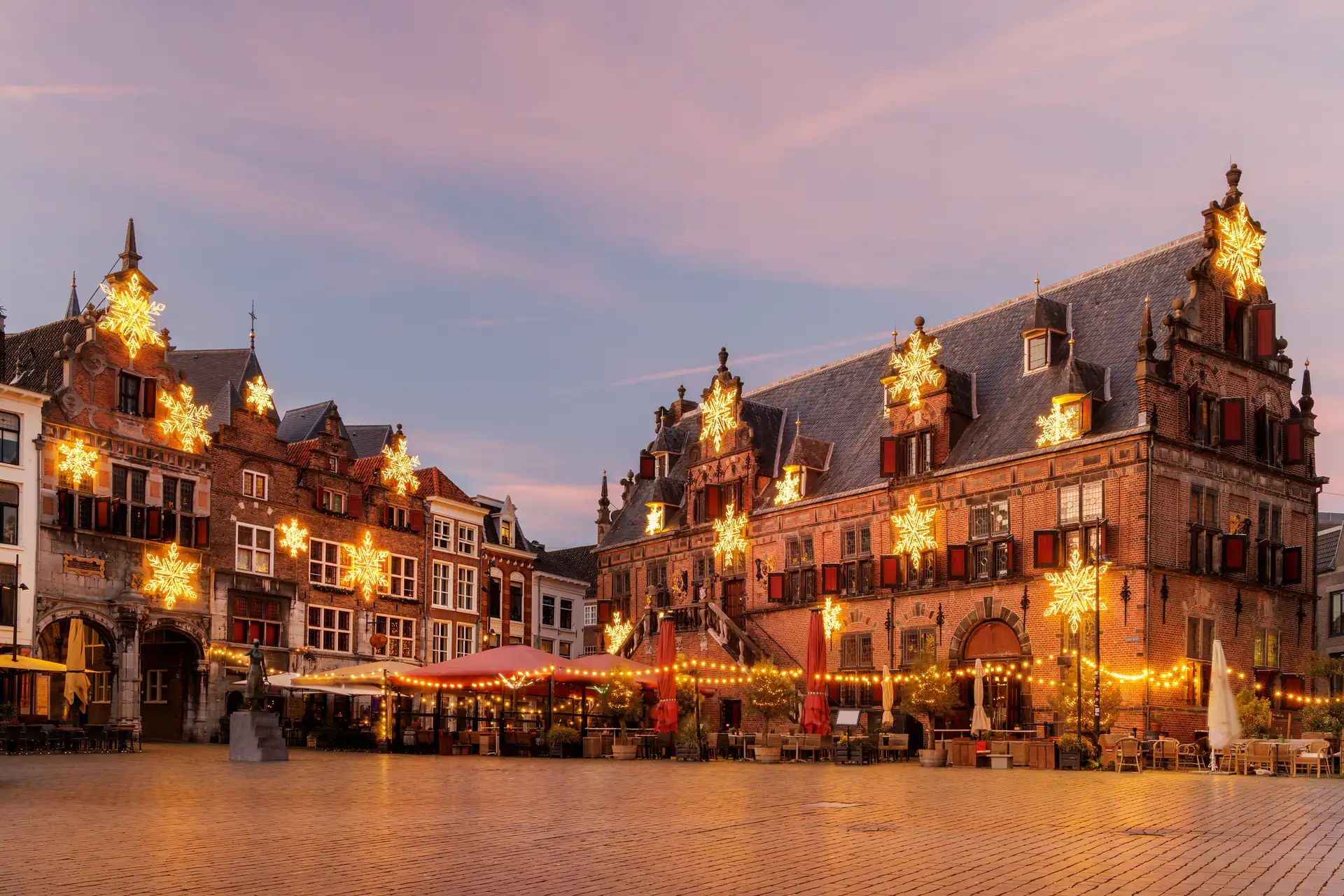 Historische Gebäude am Grote Markt mit festlichen Lichterketten und großen leuchtenden Sternen an den Fassaden bei Dämmerung in Nijmegen.