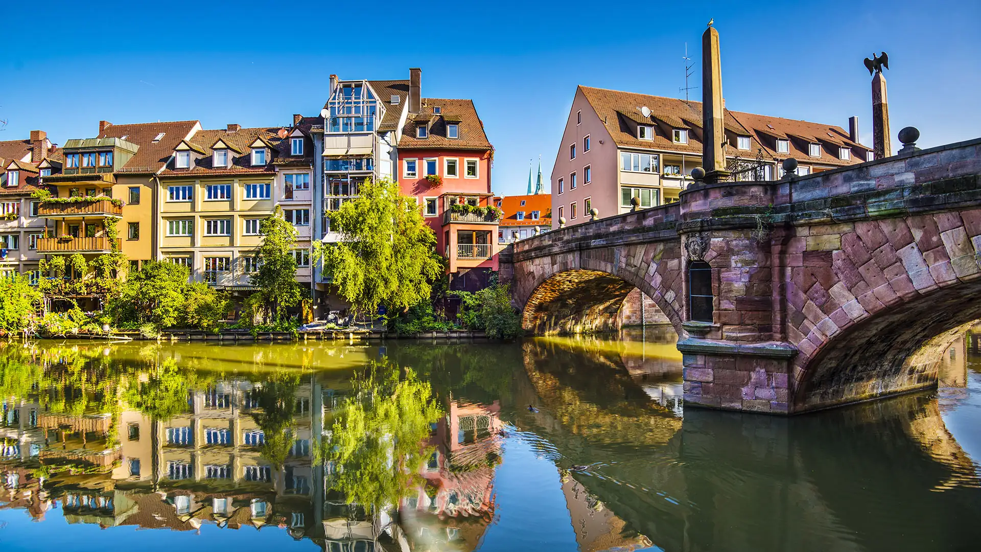 Bunte Wohnhäuser und die Maxbrücke spiegeln sich im Wasser der Pegnitz in Nürnberg