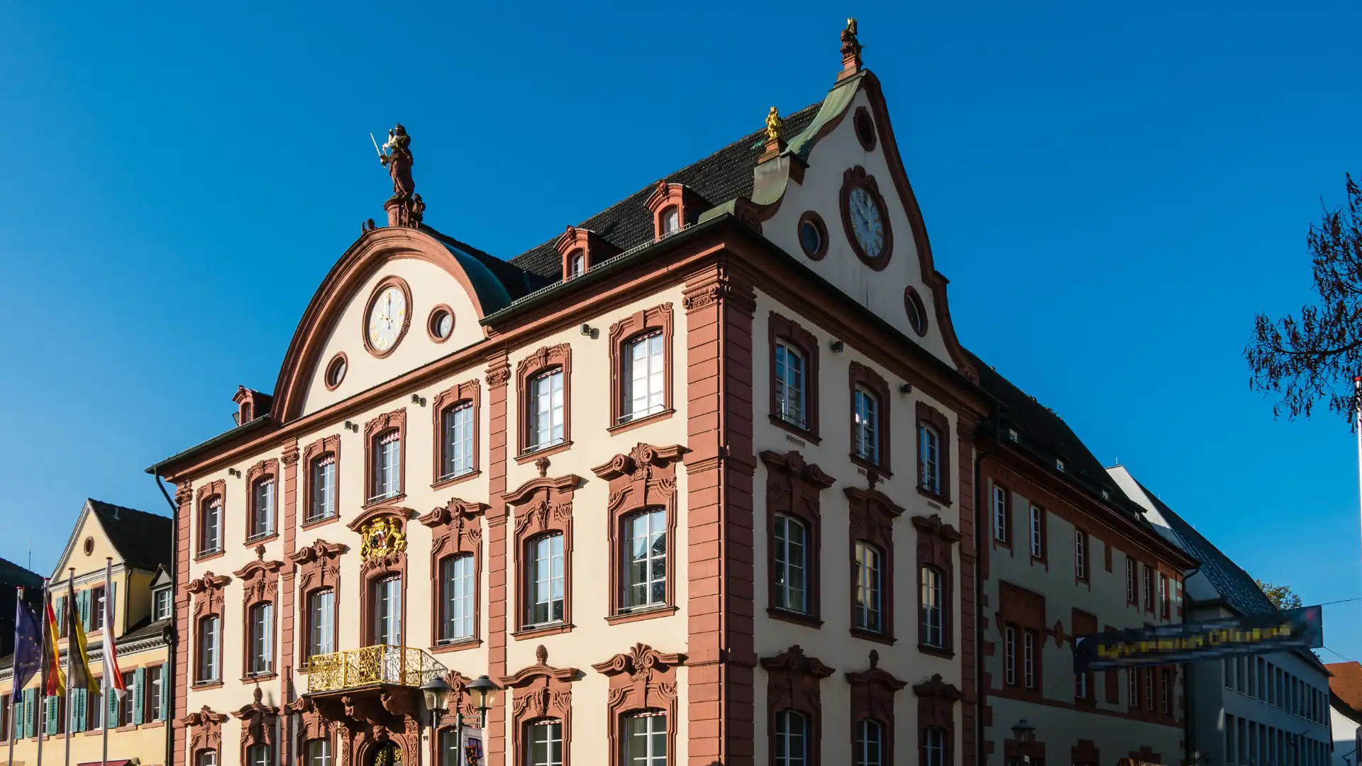 Barockes mehrstöckiges Gebäude mit reich verzierten Fenstern, goldener Balkonbrüstung und einer Statue auf dem Dachfirst