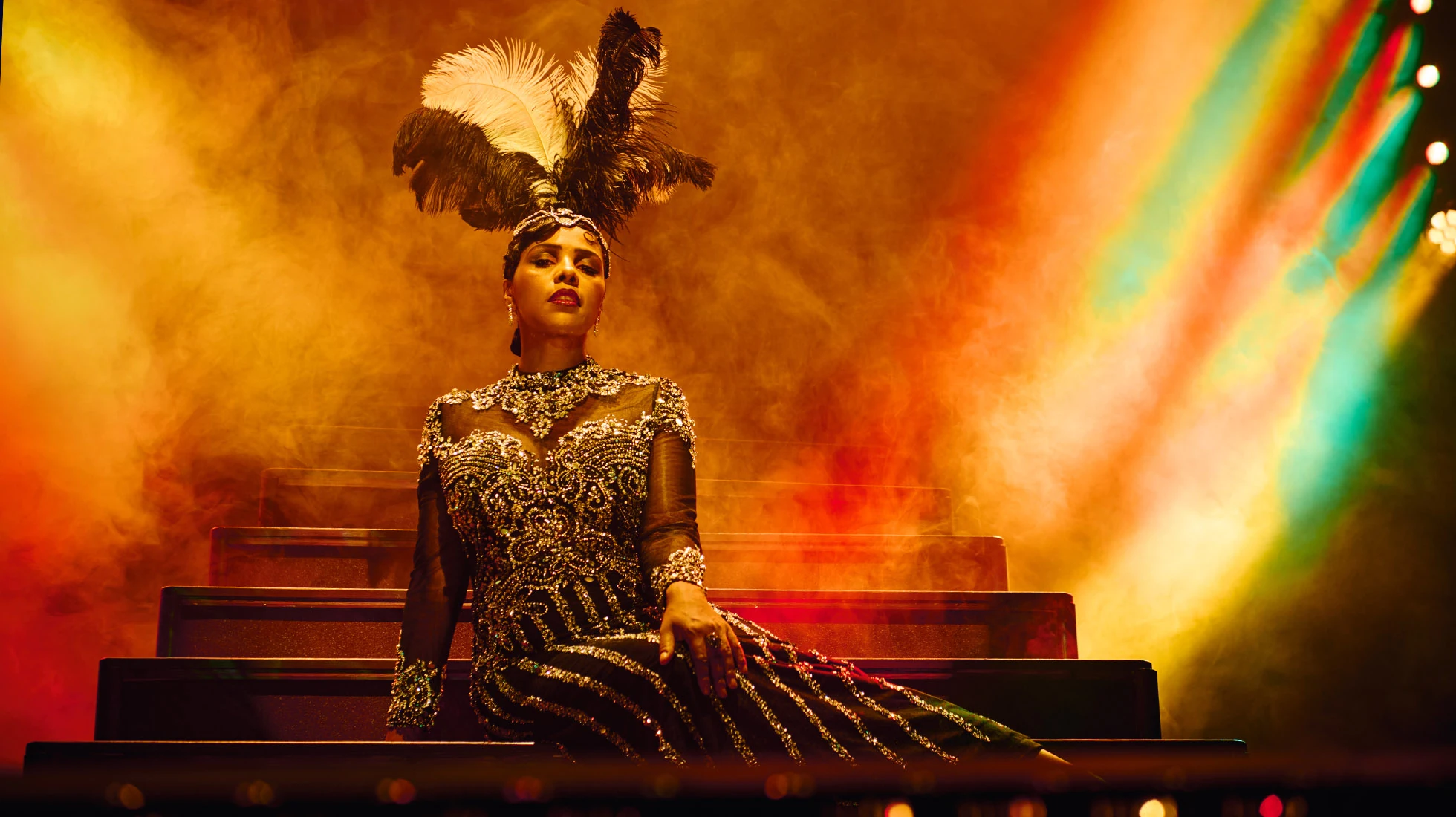 Glamouröse Darstellung einer Dame auf der Bühne, umgeben von bunten Lichtern und Nebel.