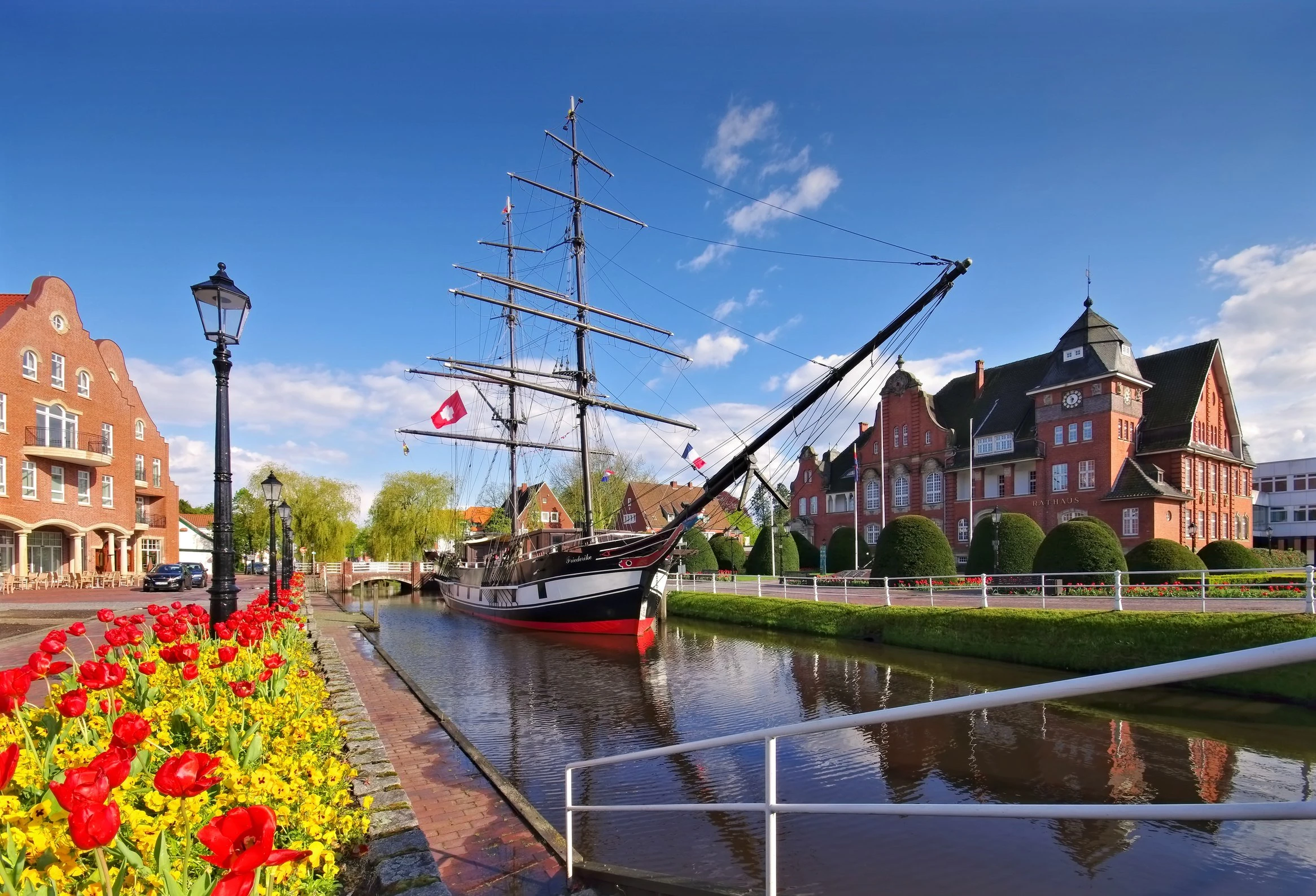 Historisches Segelschiff am Kanal in Papenburg mit roten Tulpen und Backsteingebäuden im Hintergrund
