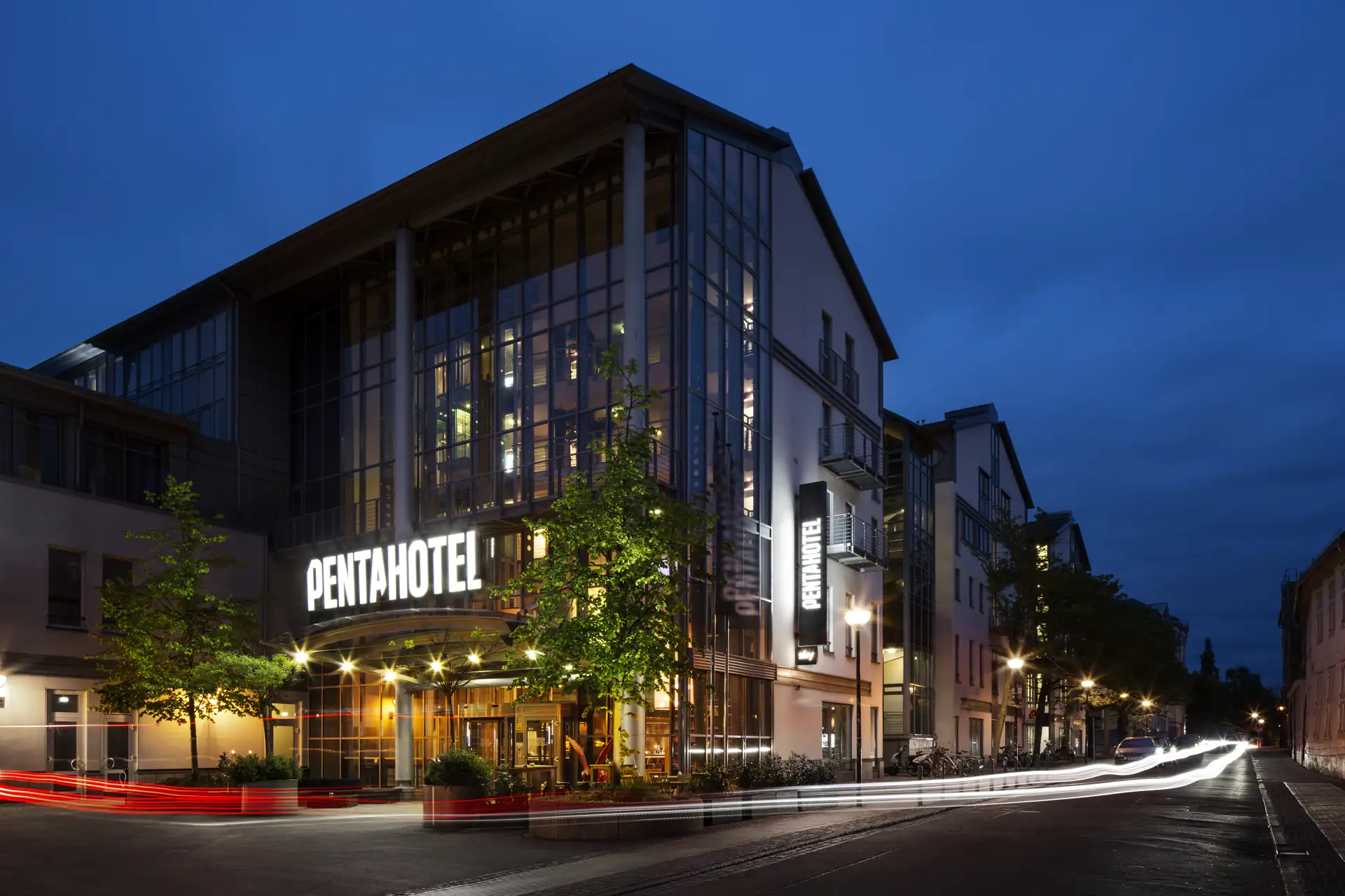 Das Penta Hotel Rostock bei Dämmerung mit beleuchtetem Schriftzug und moderner Fassade an einer Straßenecke