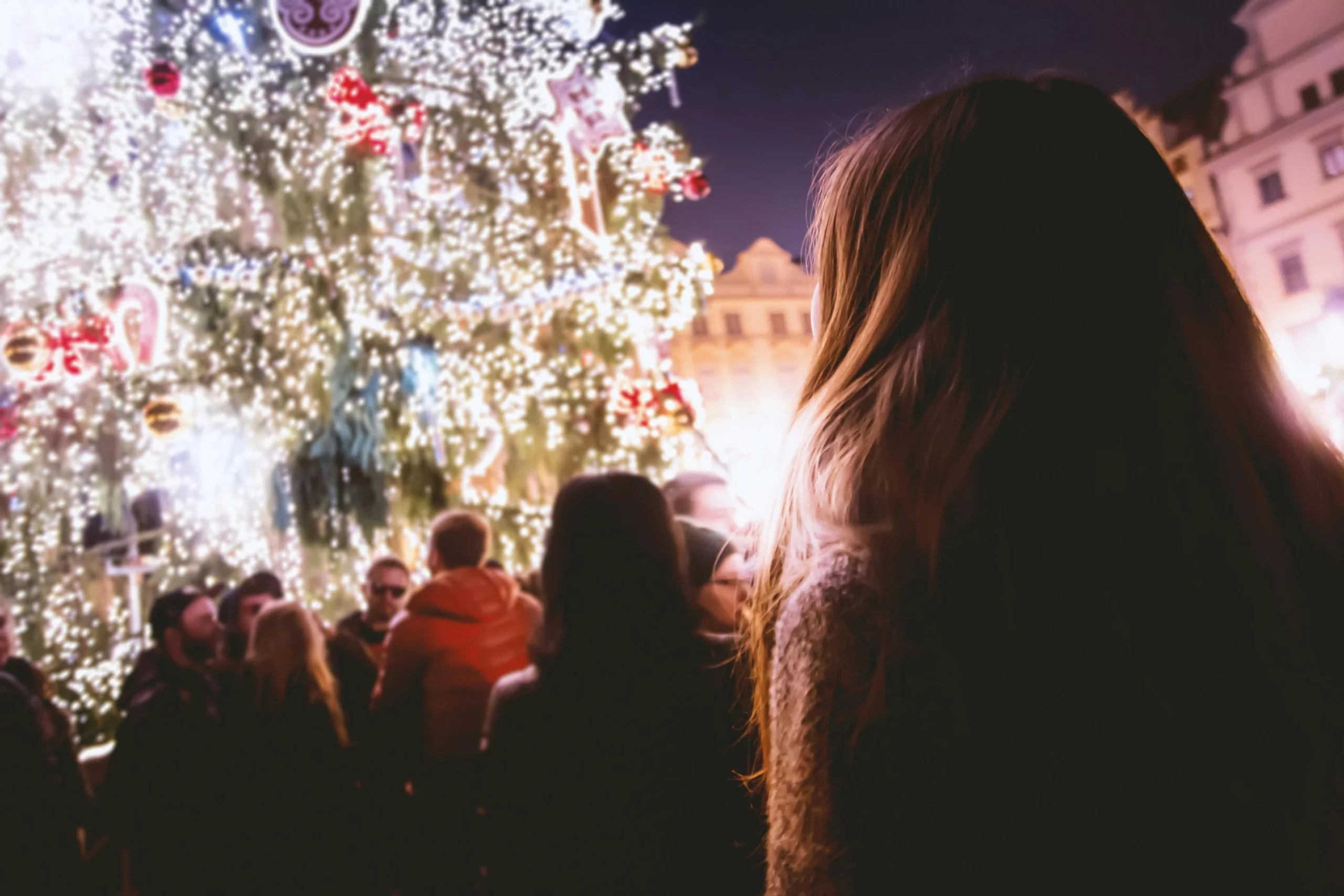 Frau steht auf Weihnachtsmarkt vor großem Baum und betrachtet diesen.