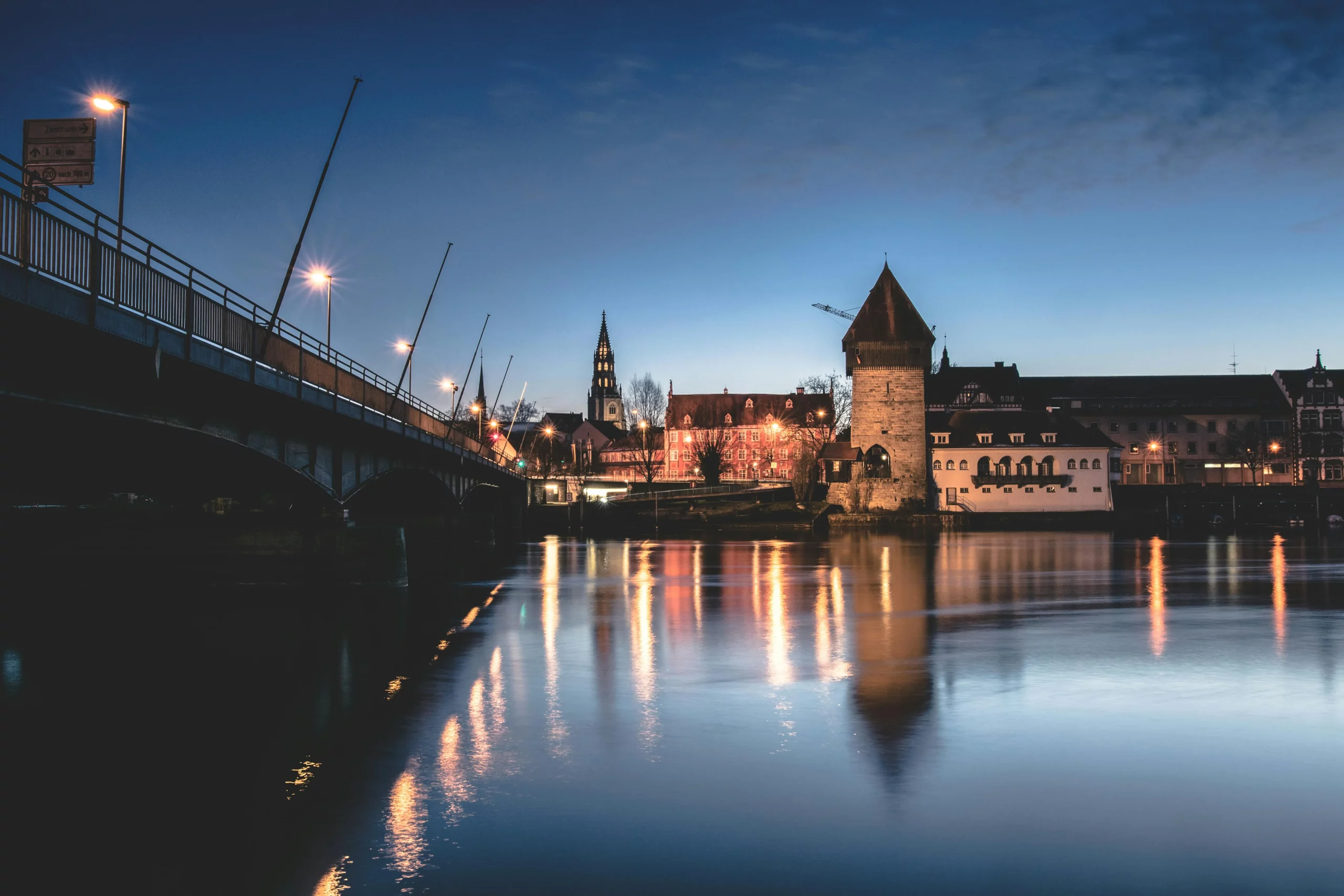 Rheintorturm und Brücke in Konstanz bei Abenddämmerung, stimmungsvoll beleuchtet mit Spiegelungen auf dem Rhein.