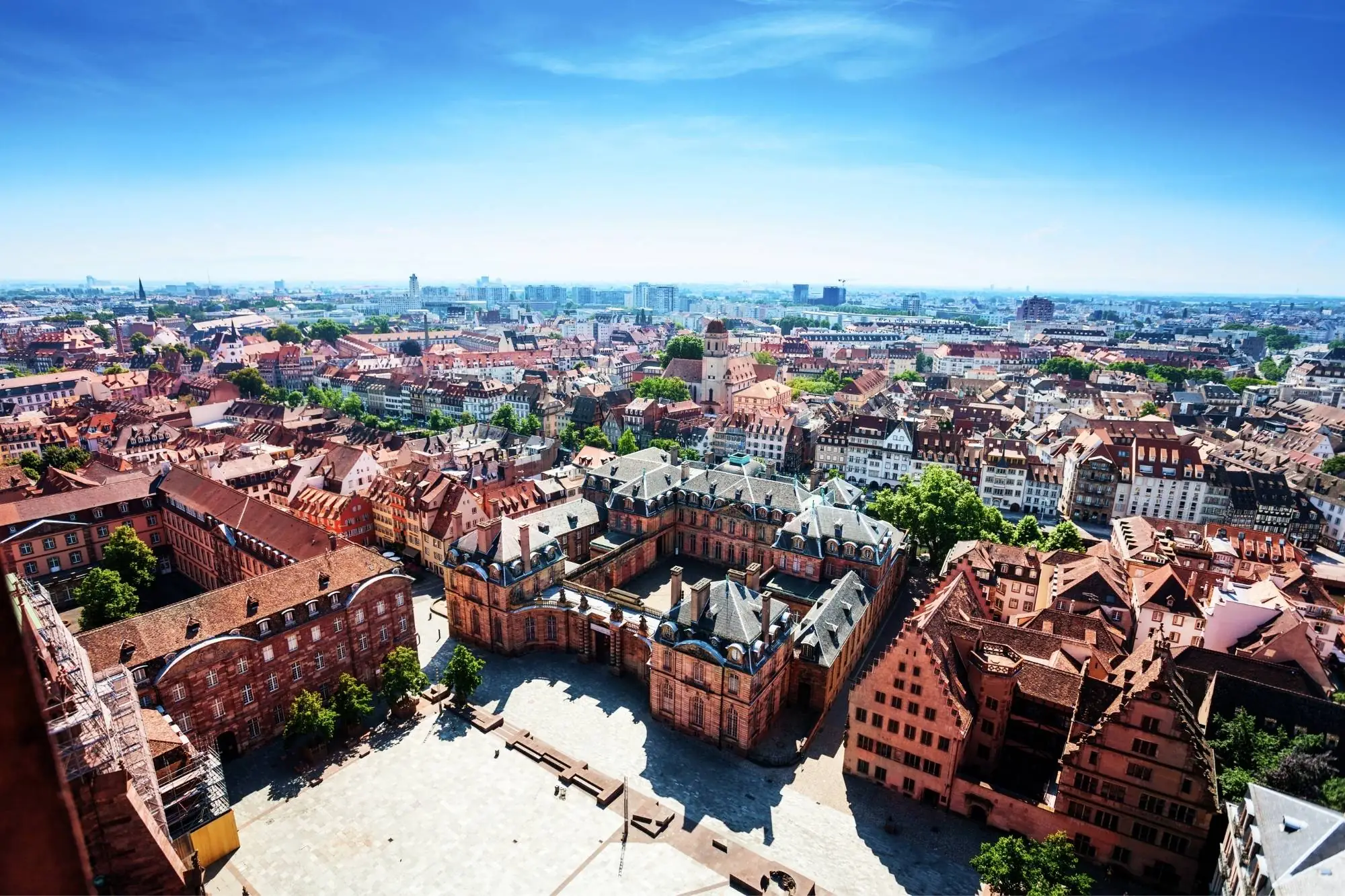 Luftaufnahme des Place du Château in Straßburg mit historischen Gebäuden, roten Dächern und weiter Stadtansicht unter blauem Himmel.