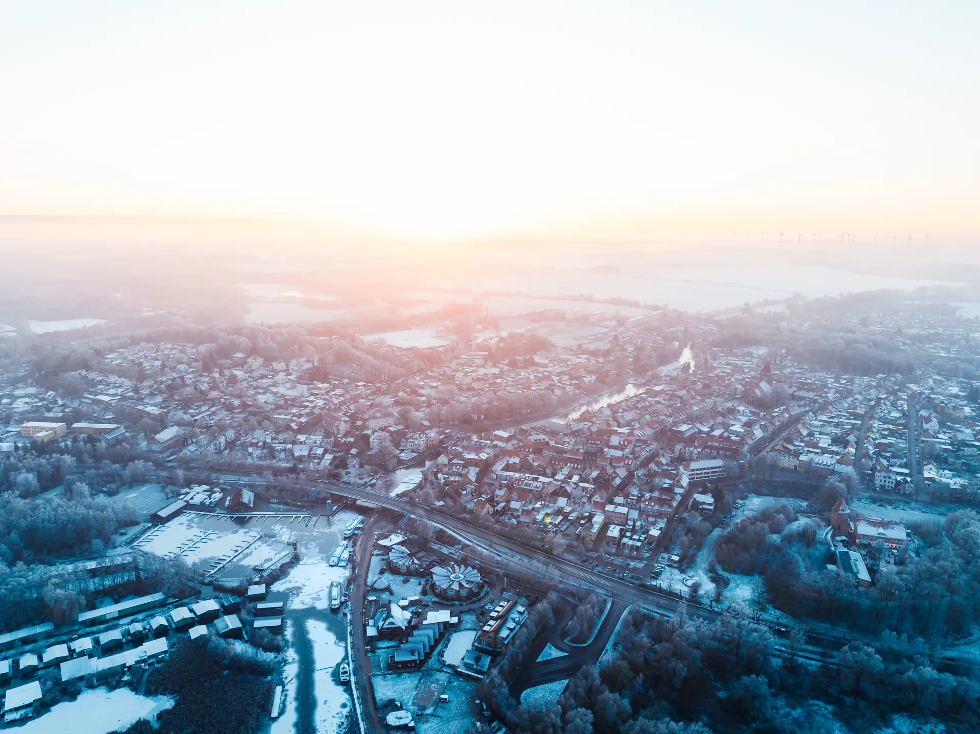 Luftaufnahme von Plau am See mit schneebedeckten Dächern und Straßen bei Sonnenaufgang.