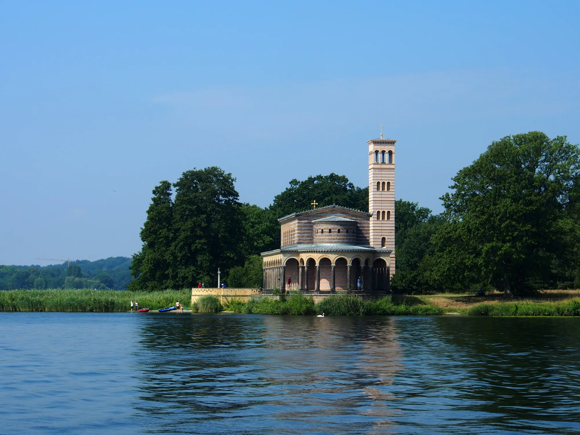 Historisches Gebäude am See mit Bäumen im Hintergrund.