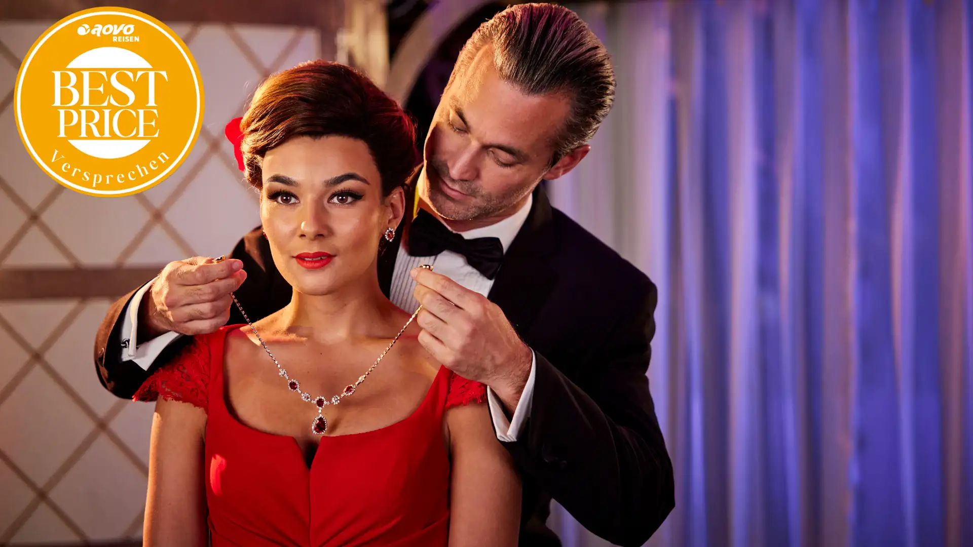 Edward (im Anzug) legt Vivian (im roten Kleid) ein Rubin besetztes Collier um (Szene aus Pretty Woman – Das Musical) mit aovo Best Price Logo