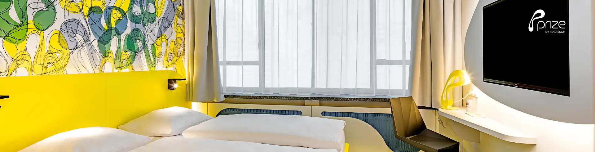 Prize Dortmund Banner: Hotelzimmer mit zwei Einzelbetten, gelber Wand, großem Fenster und modernem Fernseher an der Wand