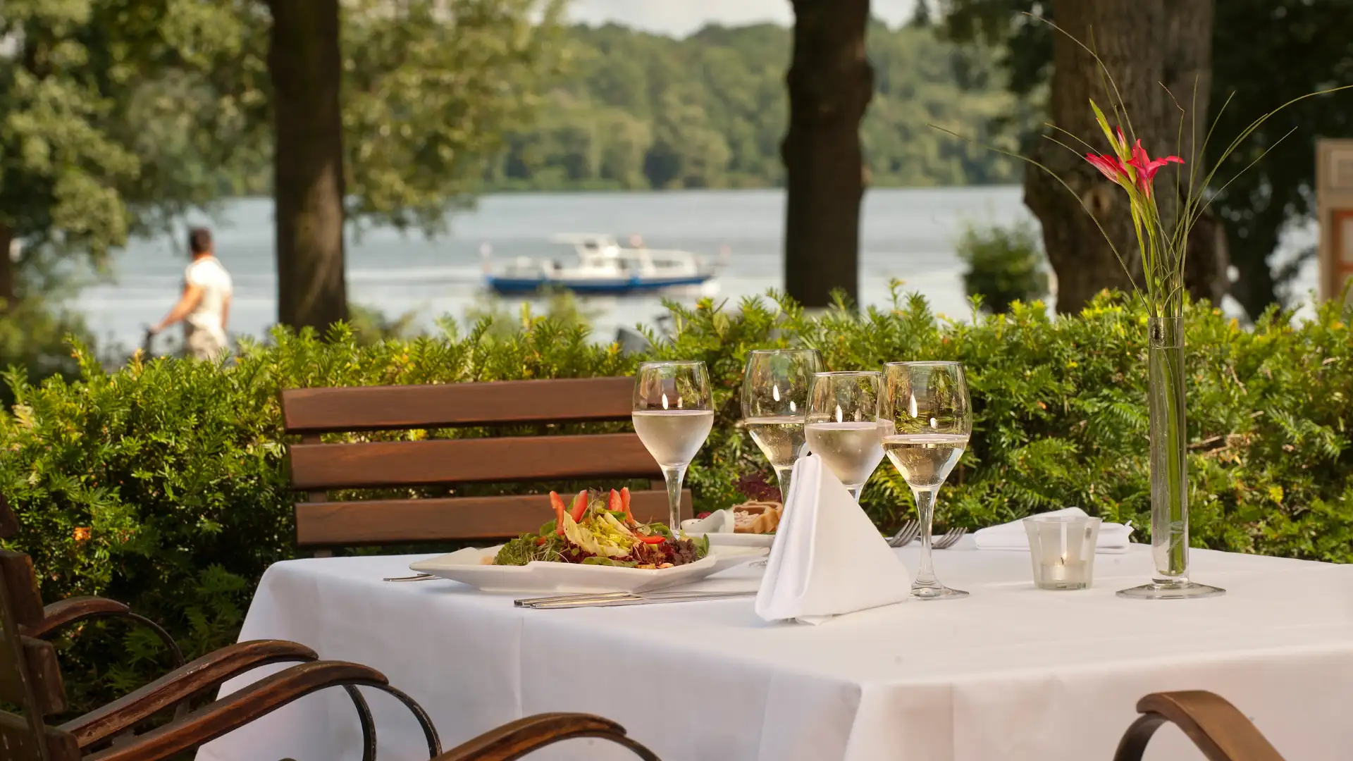 Tisch mit weißer Tischdecke, Weingläsern und Blumen vor dem Templiner See mit Boot und Bäumen im Hintergrund im Seminaris SeeHotel Potsdam