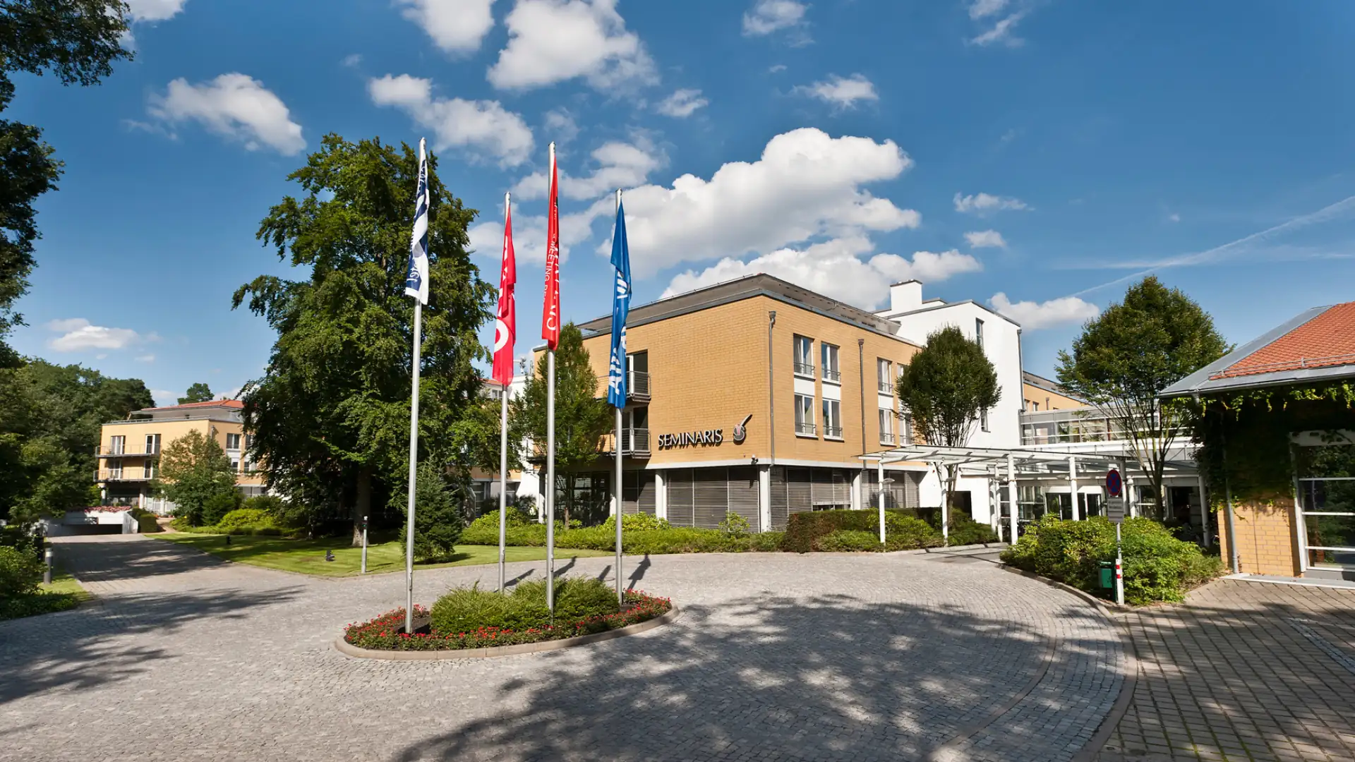 Seminaris SeeHotel Potsdam umgeben von Bäumen und Flaggen bei sonnigem Himmel
