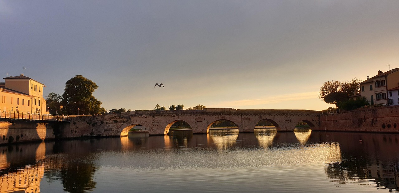 Steinbrücke mit fünf Bögen über ruhigem Wasser bei Sonnenuntergang in Rimini, Italien