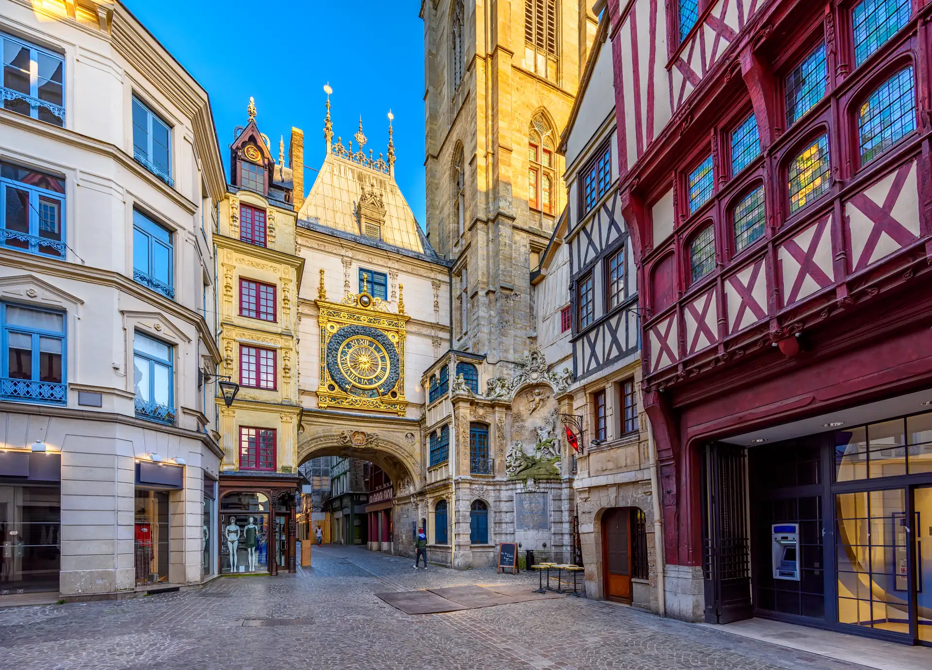 Rouen: Historisches Uhrwerk mit goldener astronomischer Uhr an einem Torbogen zwischen Fachwerkhäusern in einer gepflasterten Straße.