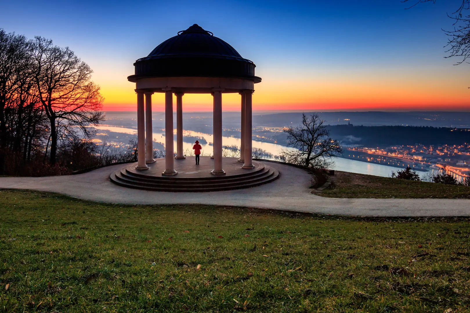 Person beobachtet vom Niederwalddenkmal in Rüdesheim den Sonnenaufgang über dem Rhein im Winter
