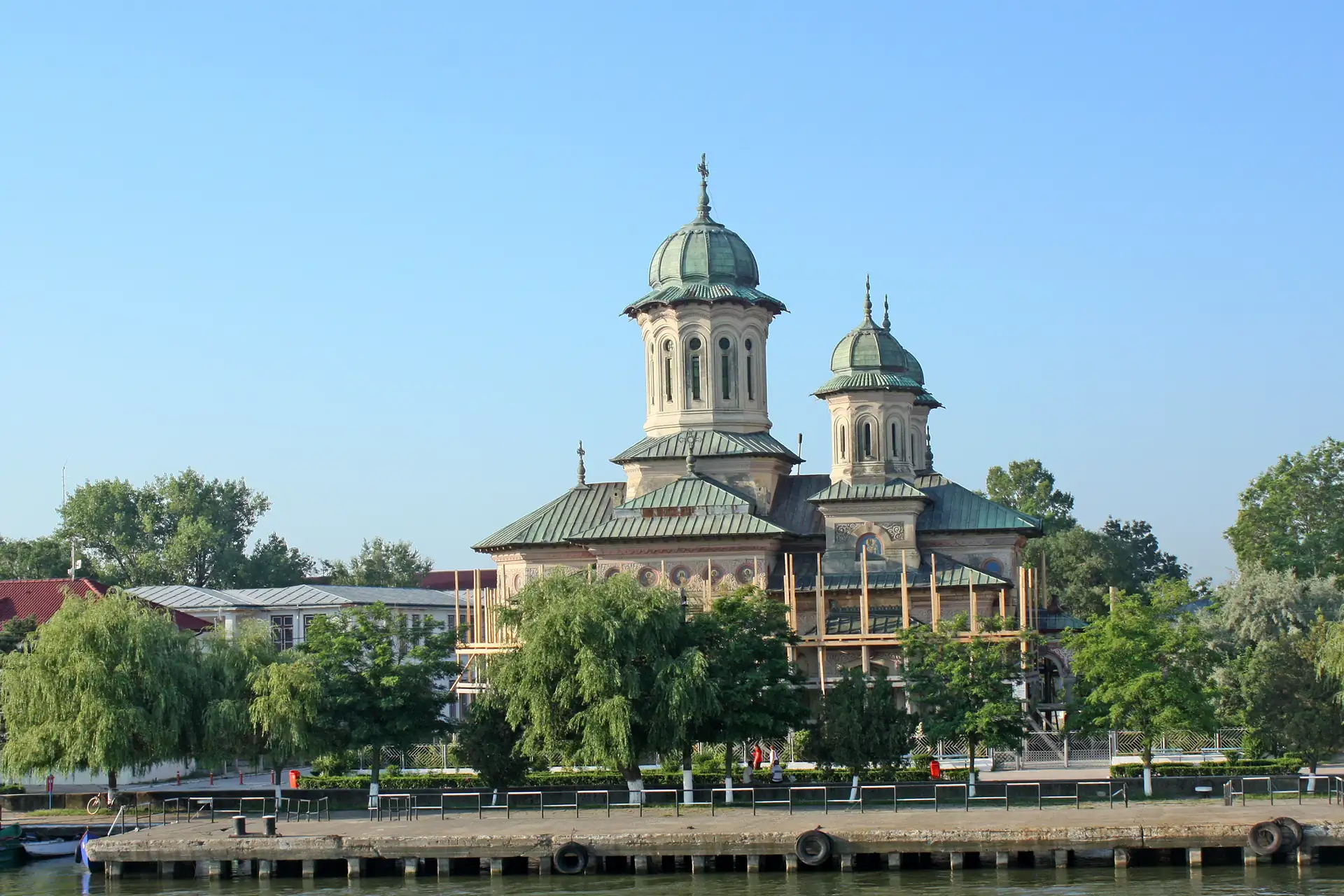 Kirchengebäude in Giurgiu mit zwei Kuppeltürmen hinter Bäumen am Flussufer bei klarem Himmel