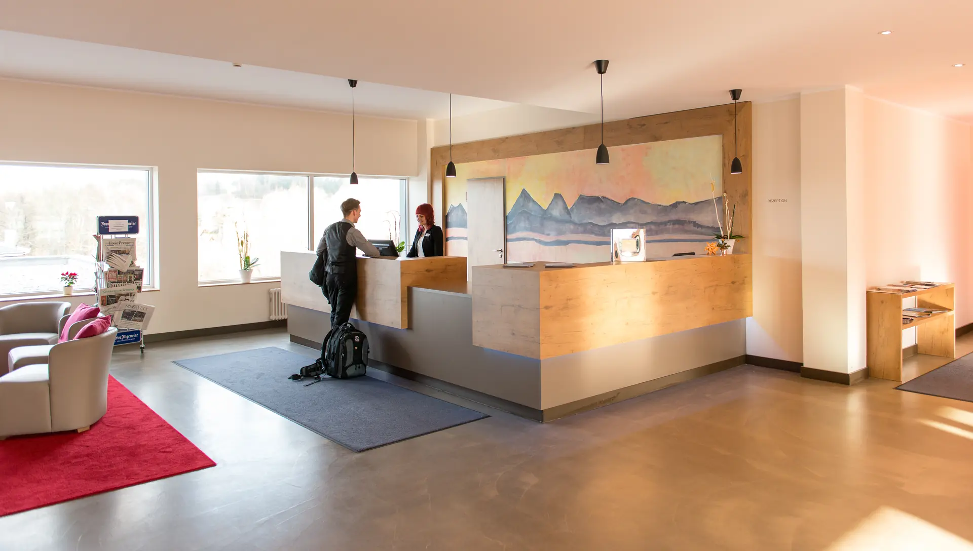 Empfangstresen mit Hotelpersonal und Gast im Santé Royale Hotel- & Gesundheitsresort Warmbad Wolkenstein