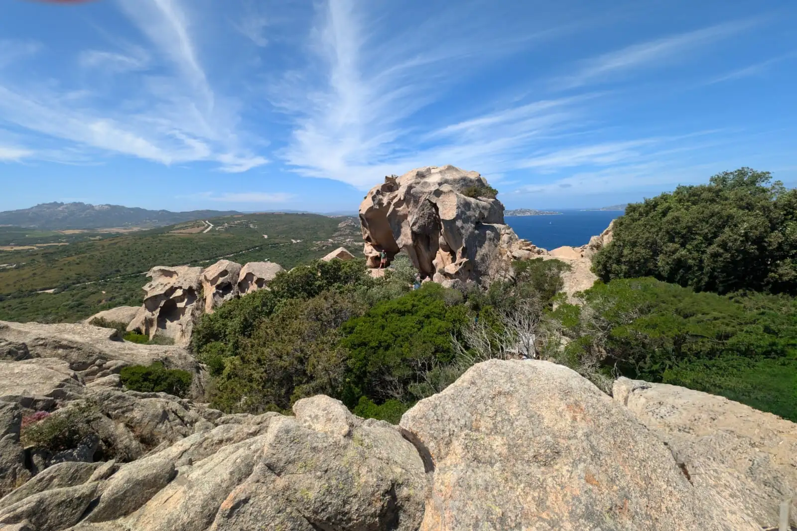 Felsformationen Capo d'Orso (Bärenfelsen) und grüne Büsche unter blauem Himmel mit weißen Wolken am Küstengebiet auf Sardinien