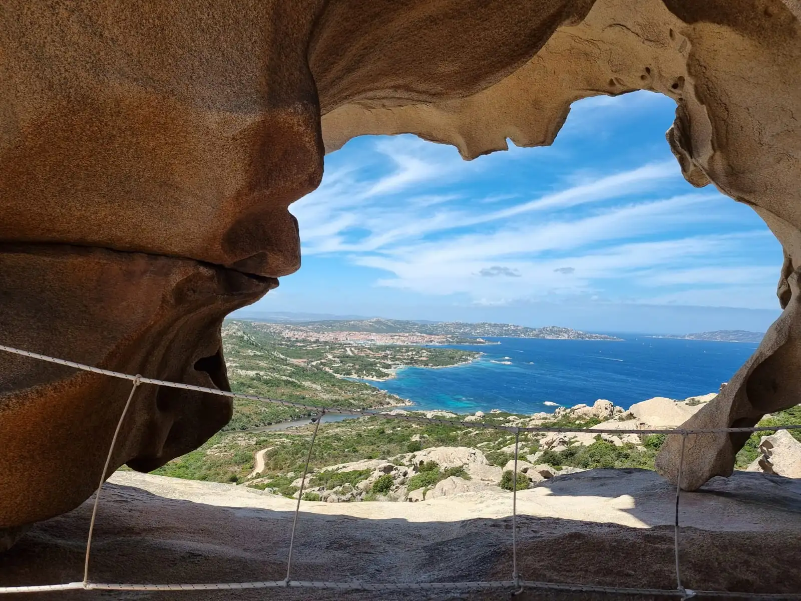 Näherer Blick durch die Felsöffnung am Capo d'Orso (Bärenfelsen) auf die Küstenlandschaft mit blauem Meer und Himmel auf Sardinien (im Querformat)