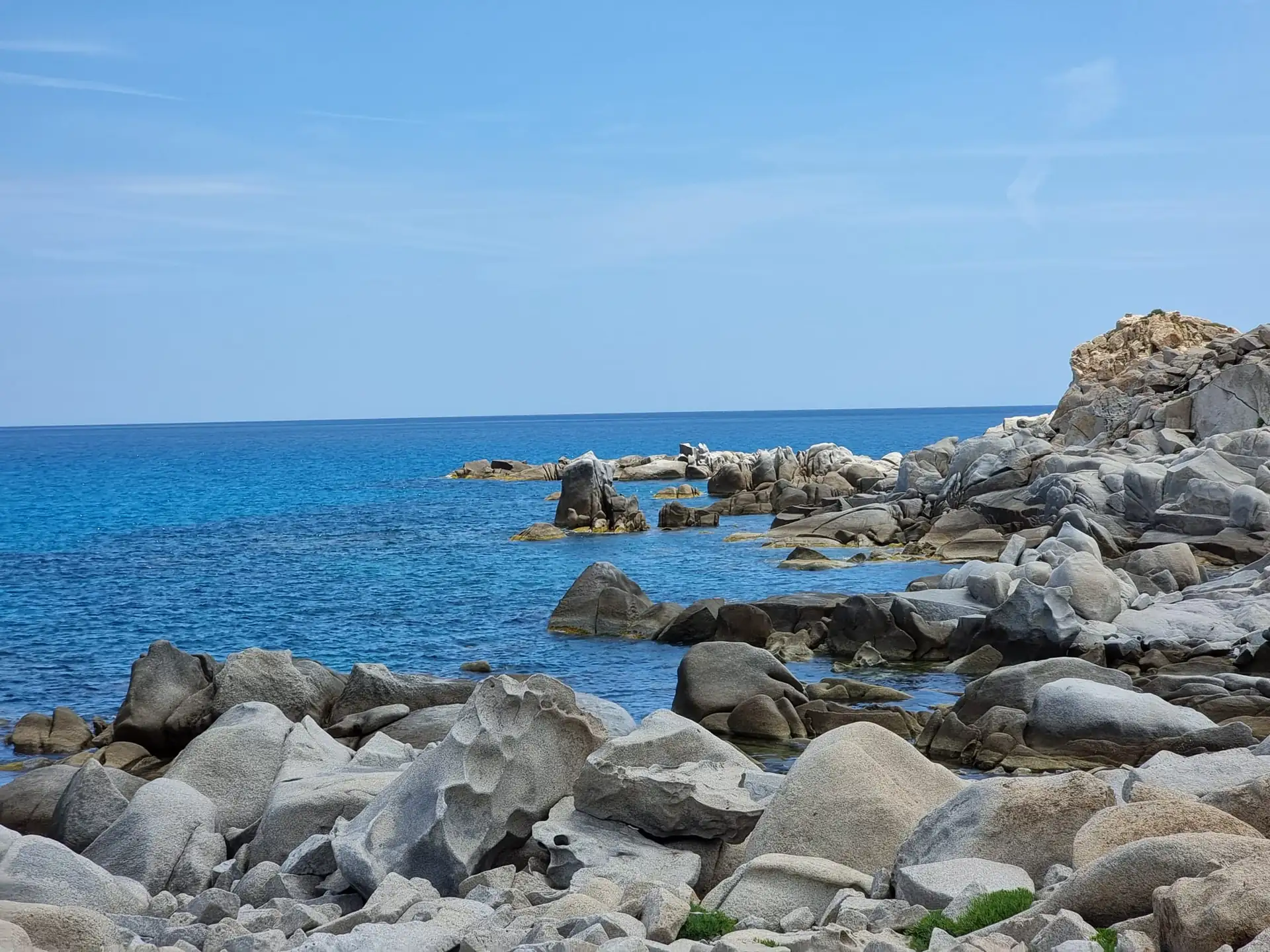 Felsige Küste mit großen grauen Steinen und klarem blauem Meer unter hellem Himmel auf Sardinien